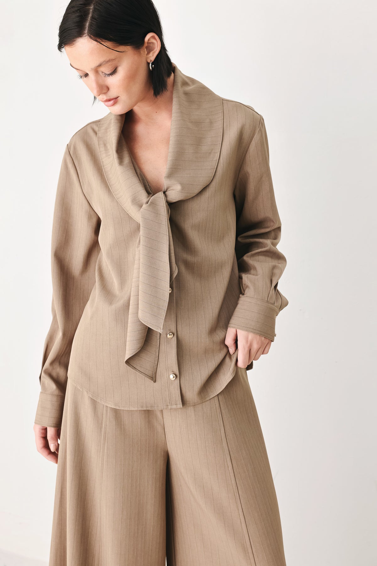 A woman wearing a taupe-beige long-sleeve button-front blouse with a large draped collar | FREEMARKET