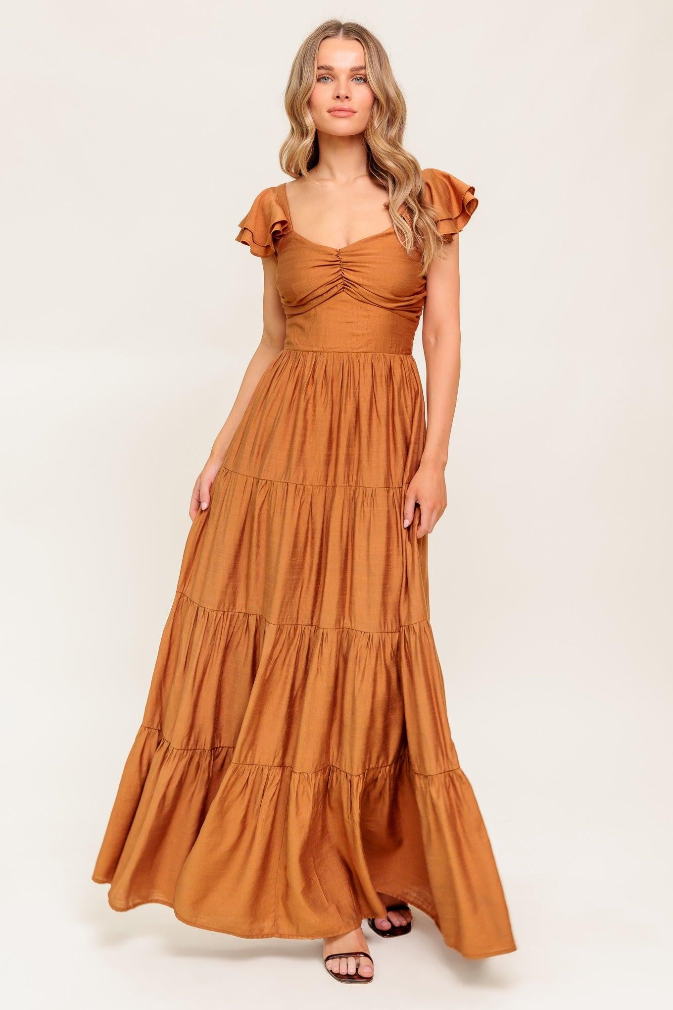 A solid woven maxi dress featuring cami top with layered sleeve, cinched front bodice, tiered skirt and smocked back bodice.