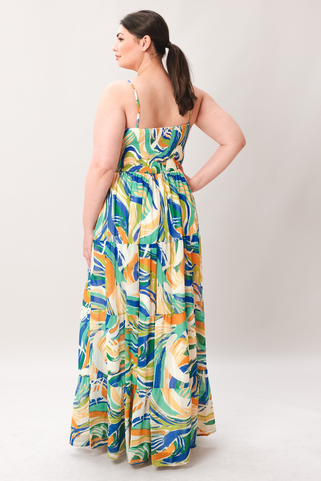 Woman wearing a colorful patterned maxi dress featuring cami bodice with front tie and cut out detail, tiered skirt and smocked back bodice on a plain background | Curve | Flying Tomato