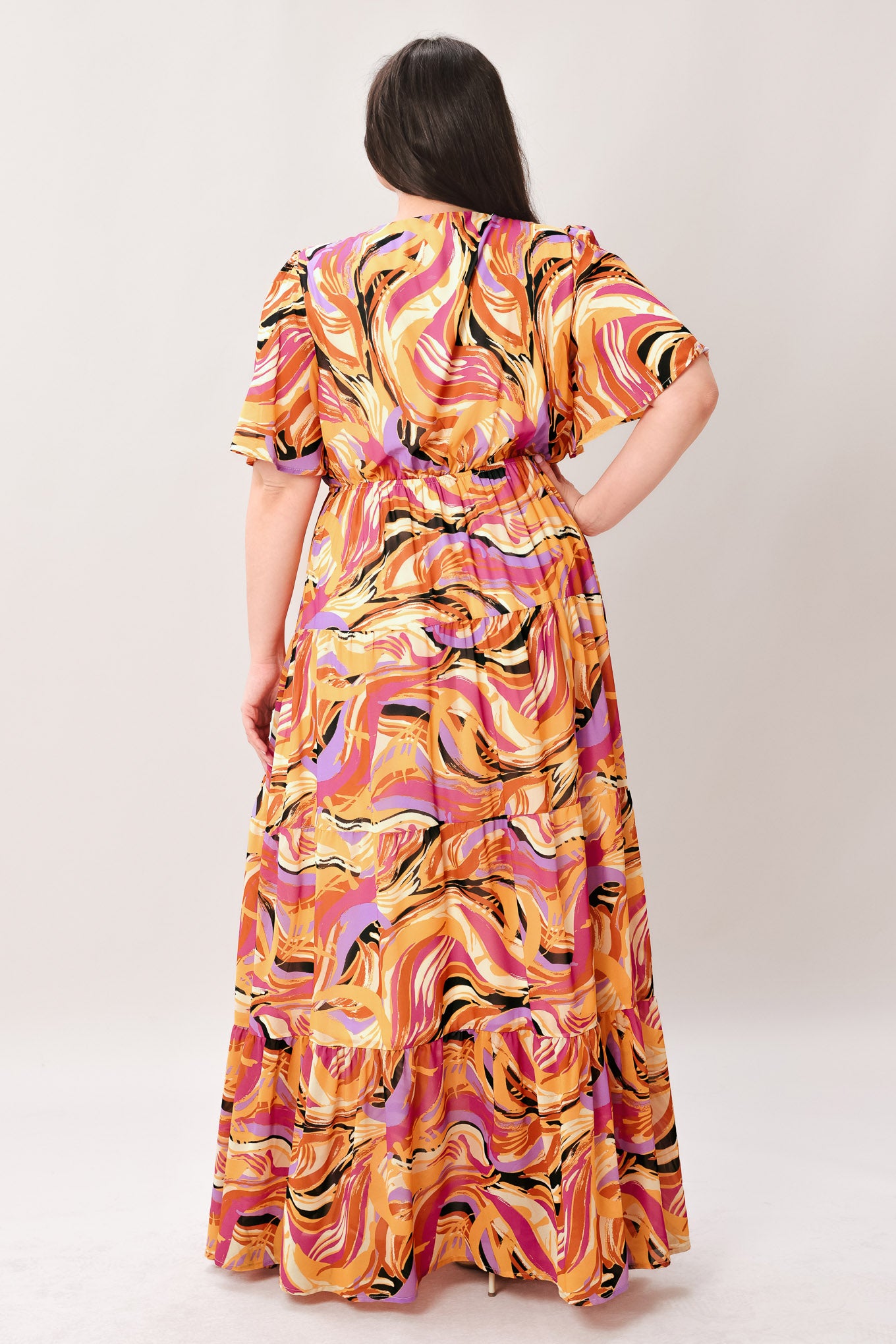 Woman wearing a colorful patterned jumpsuit featuring shirt collar, button down, long sleeve, elasticized waist, self sash tie, side pockets and wide leg on a white background | Flying Tomato