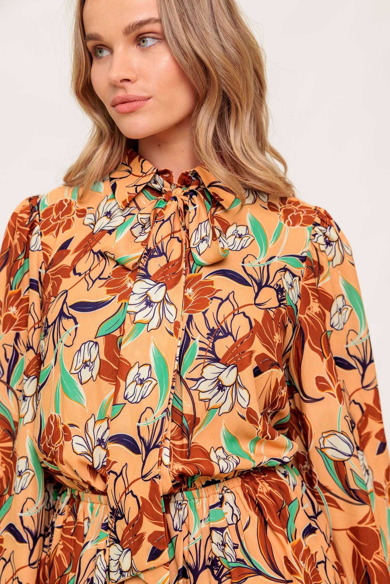 Woman wearing a floral blouse with orange and brown tones.