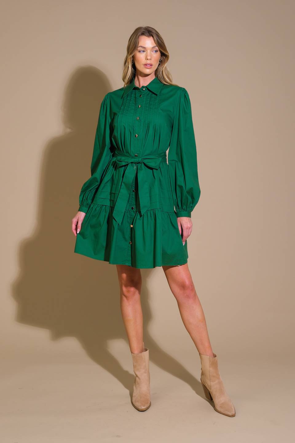 A solid woven mini dress featuring a shirt collar, button down, front pleats, long sleeve, self-sash tie, and ruffled hemline