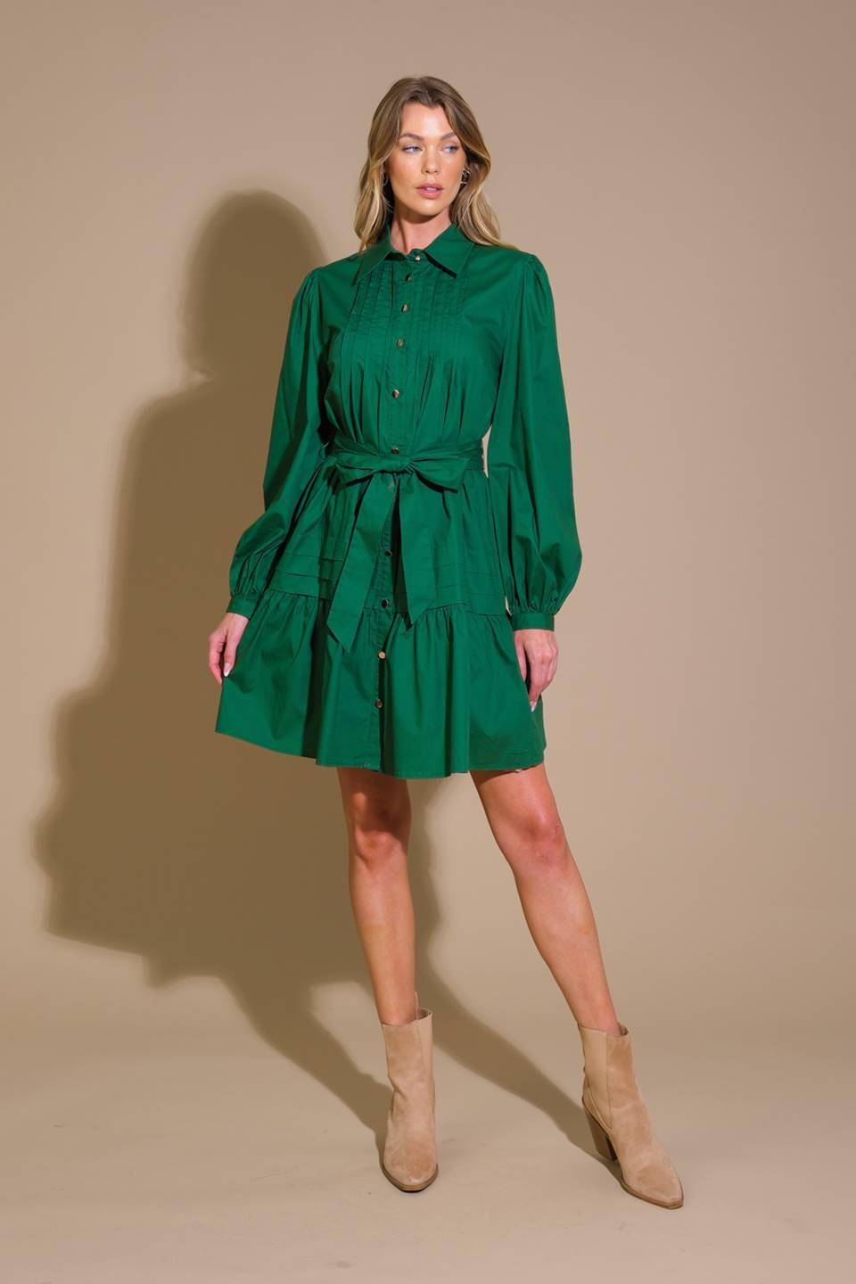 A solid woven mini dress featuring a shirt collar, button down, front pleats, long sleeve, self-sash tie, and ruffled hemline