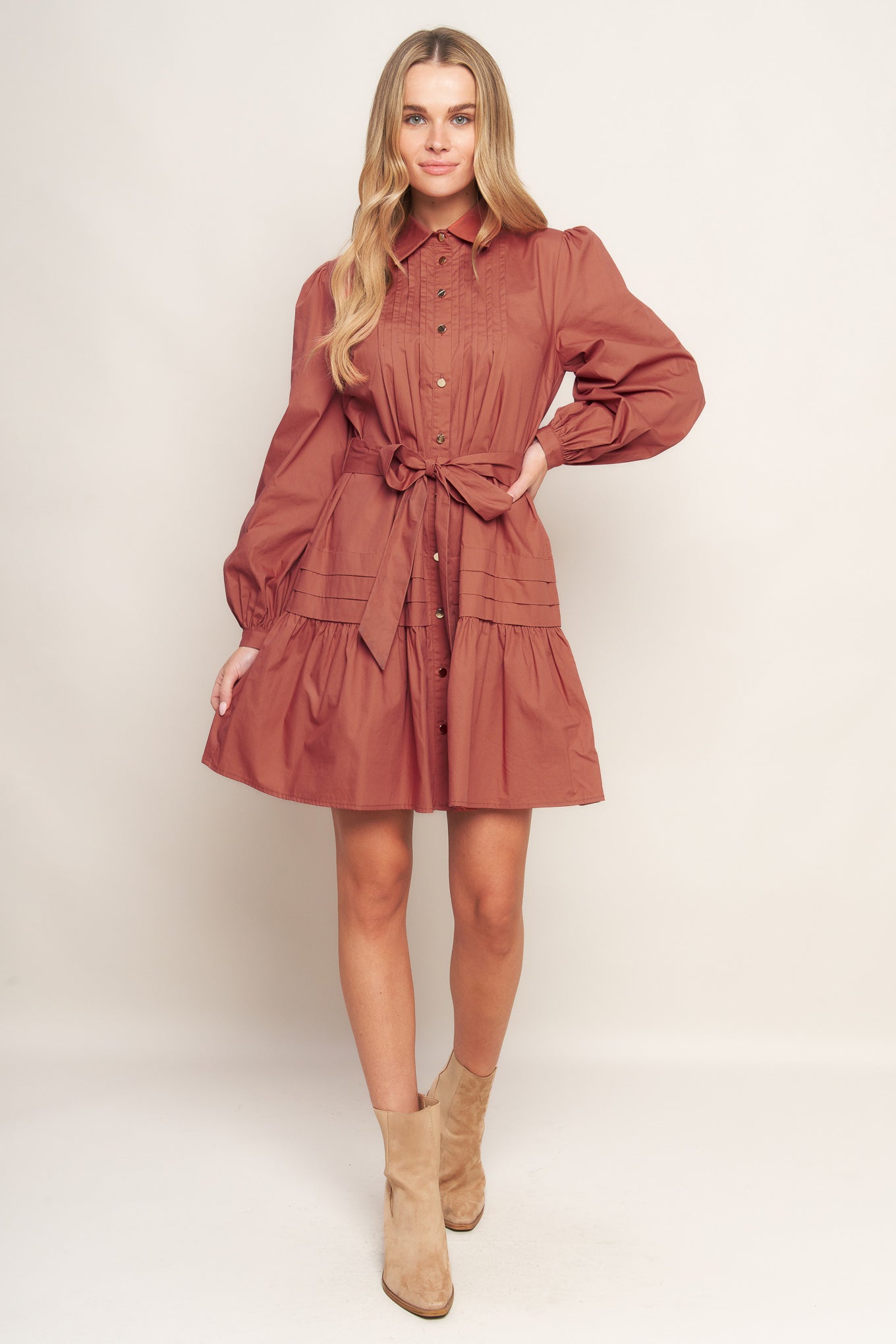 A solid woven mini dress featuring a shirt collar, button down, front pleats, long sleeve, self-sash tie, and ruffled hemline