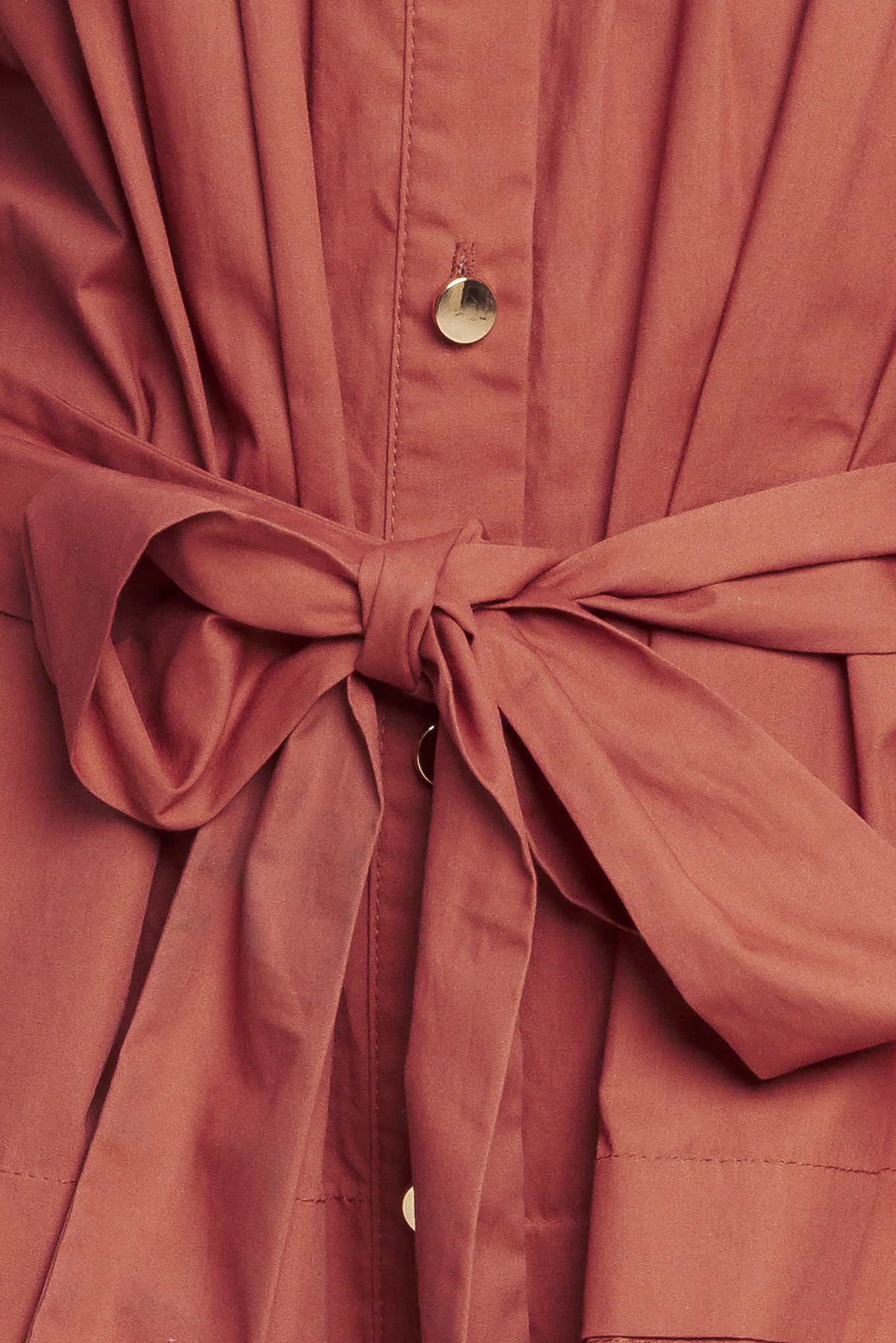 A solid woven mini dress featuring a shirt collar, button down, front pleats, long sleeve, self-sash tie, and ruffled hemline