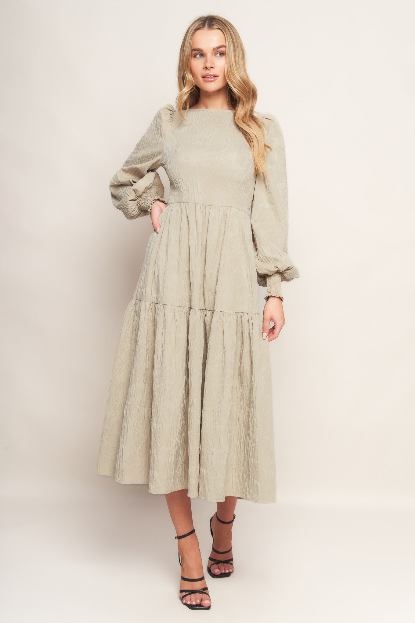 A textured woven midi dress featuring wide neckline, long sleeve with smocked cuff, tiered skirt and back zipper closure