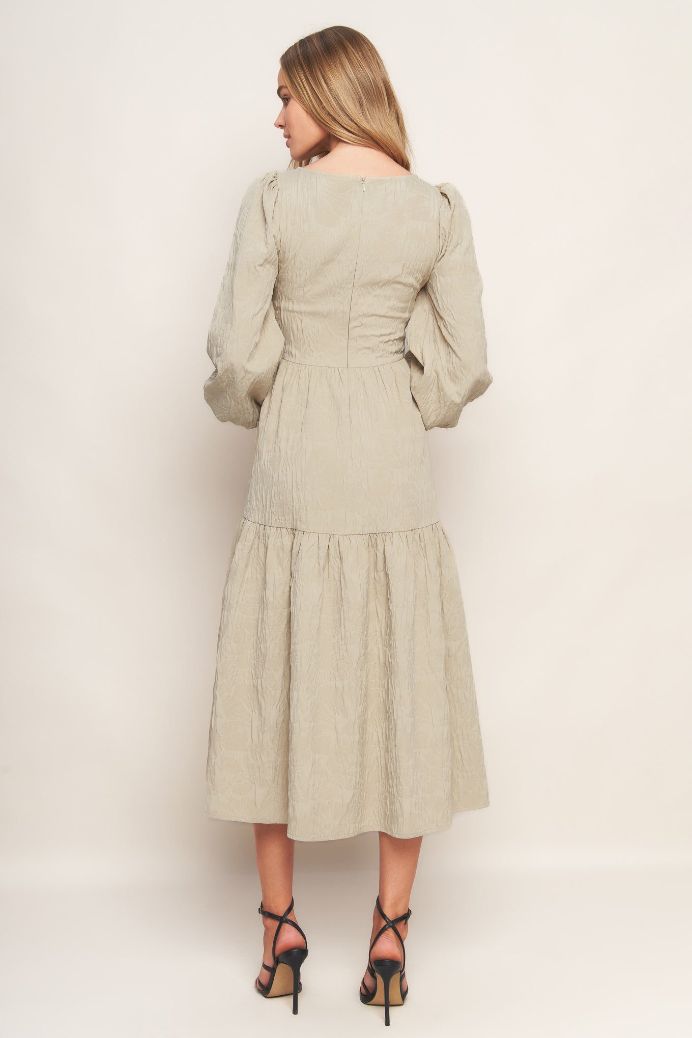 A textured woven midi dress featuring wide neckline, long sleeve with smocked cuff, tiered skirt and back zipper closure