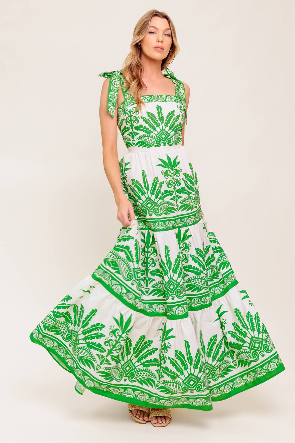 A printed woven maxi dress featuring straight neckline, shoulder tie, tiered skirt and back zipper closure.
