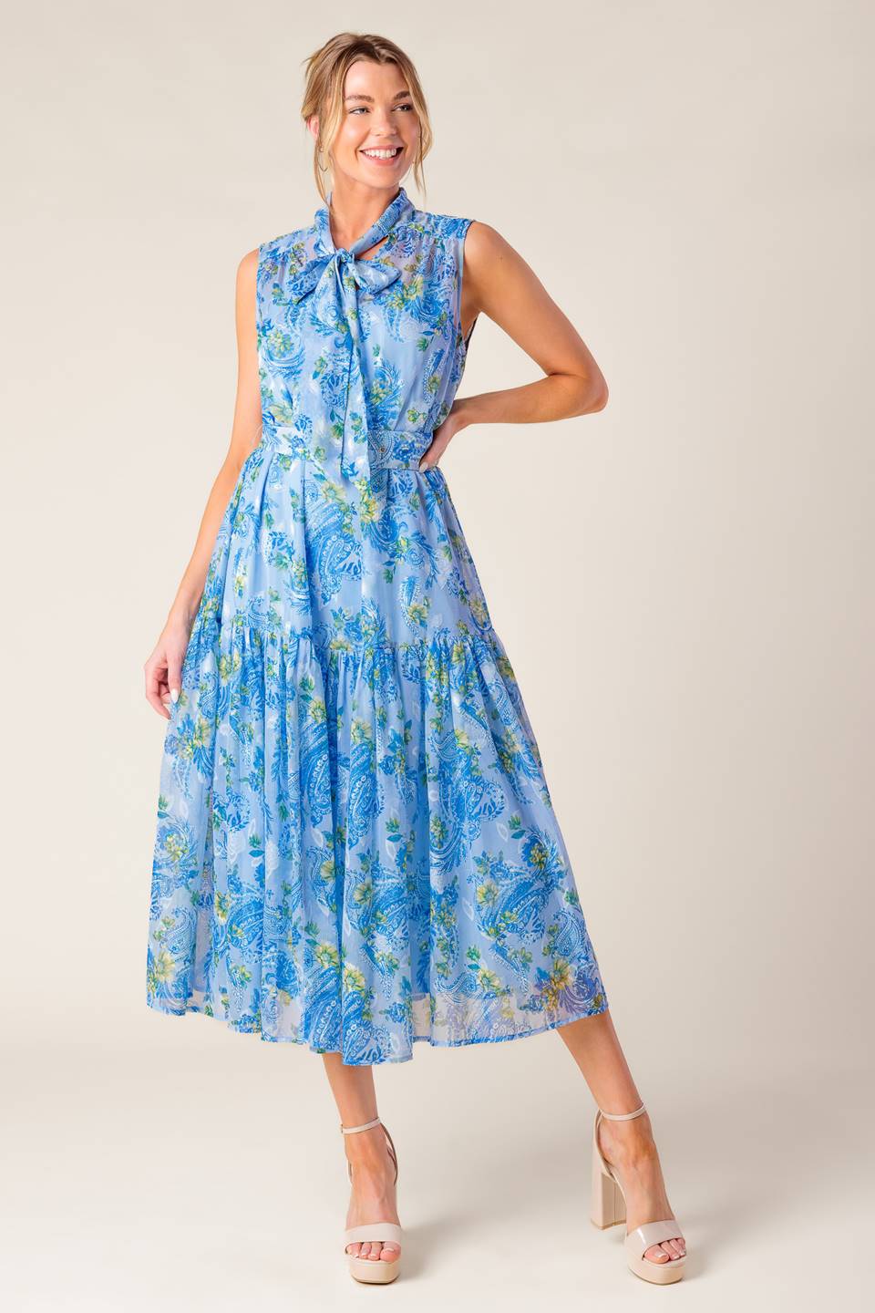 A printed woven midi dress featuring front bow tie, sleeveless, self belt and ruffled hemline