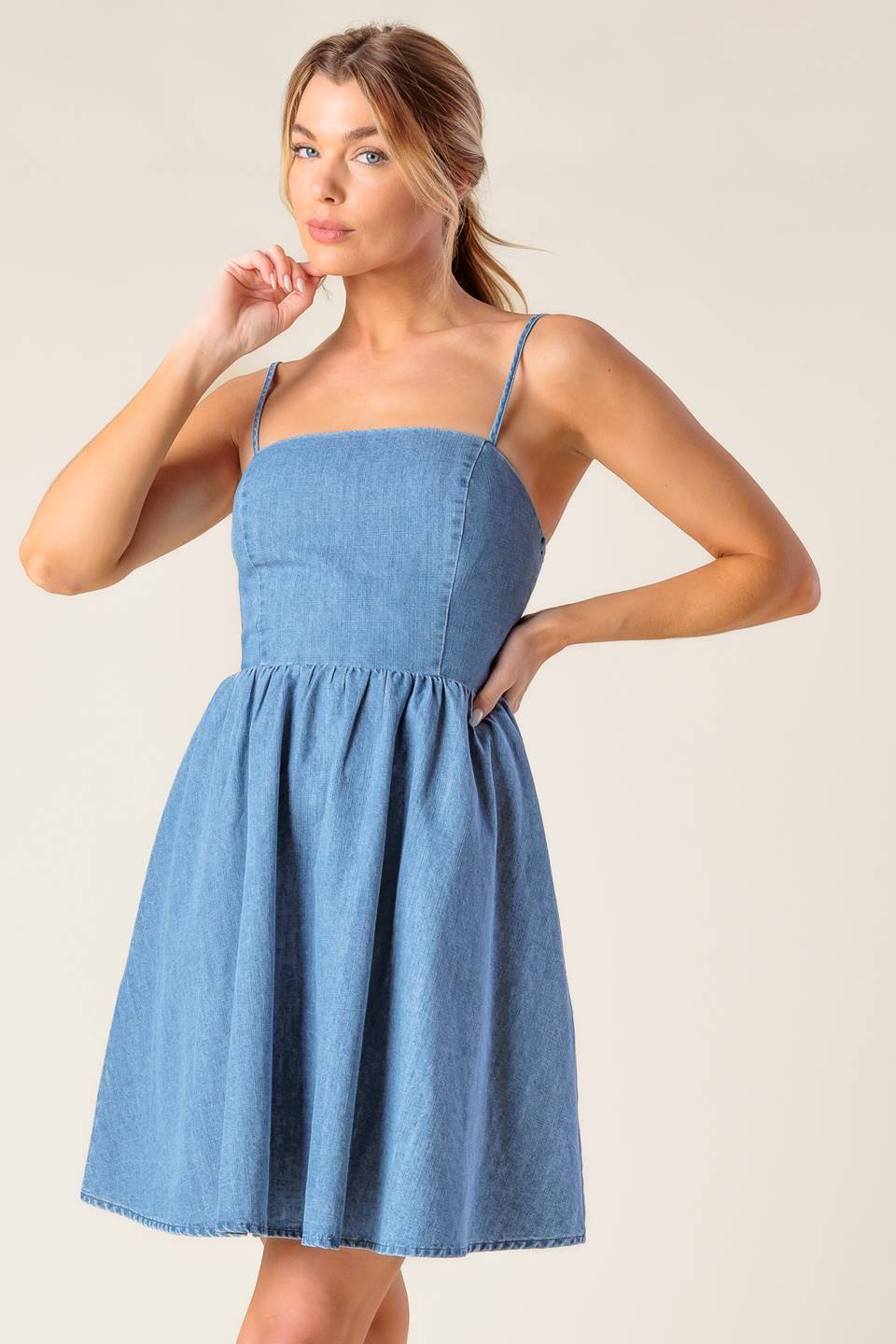 A washed denim mini dress featuring straight neckline, straps, full skirt and smocked back with cut out