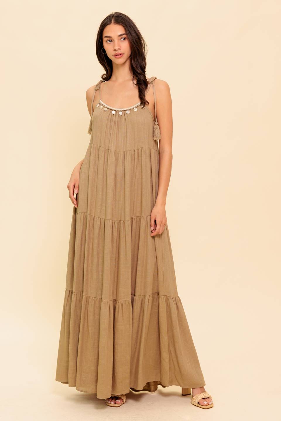 A solid woven maxi dress featuring shoulder tie with tassel, front neck trim and tiered skirt