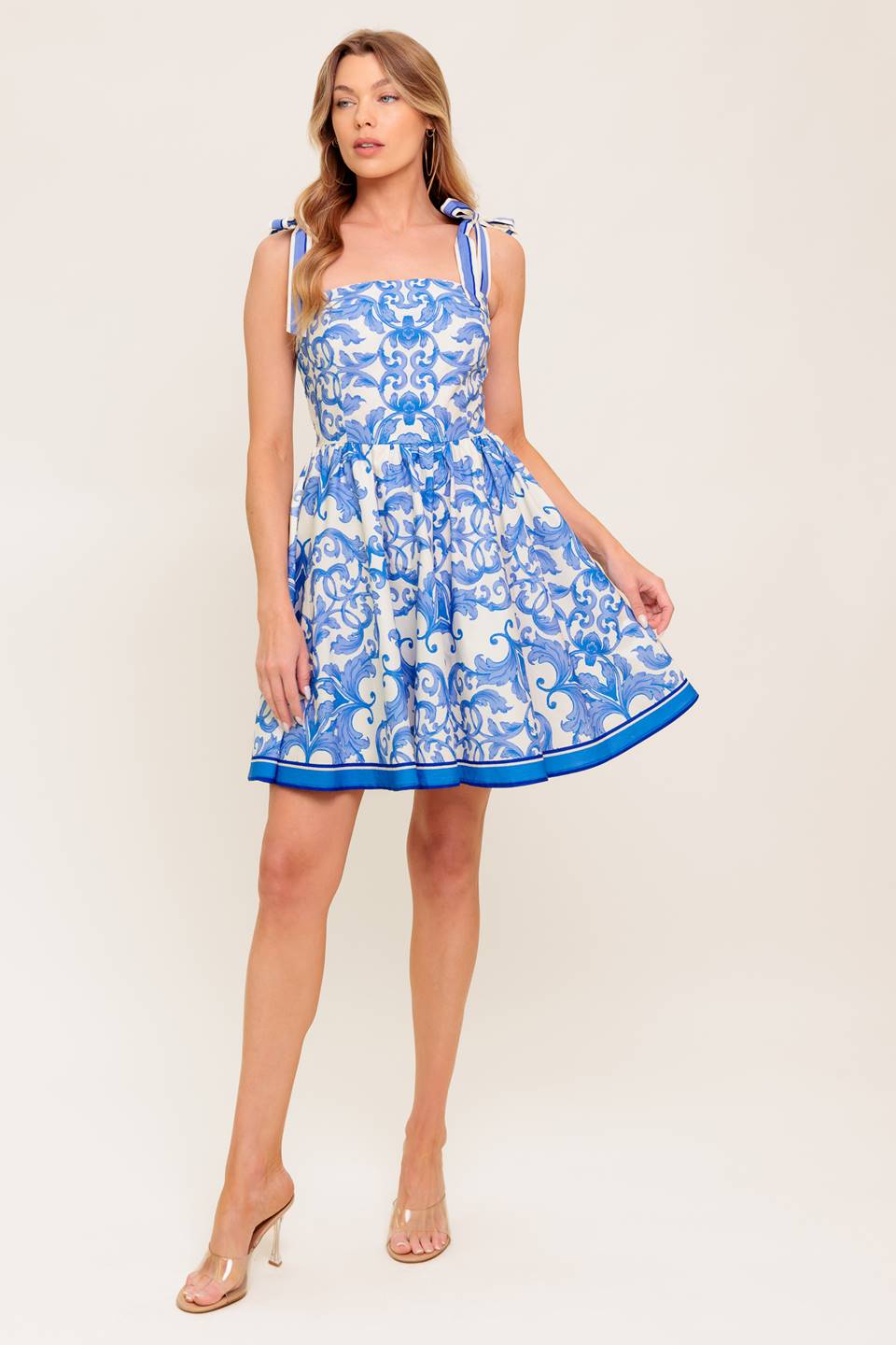 A printed woven mini dress featuring straight neckline, shoulder tie, full skirt and smocked back bodice.