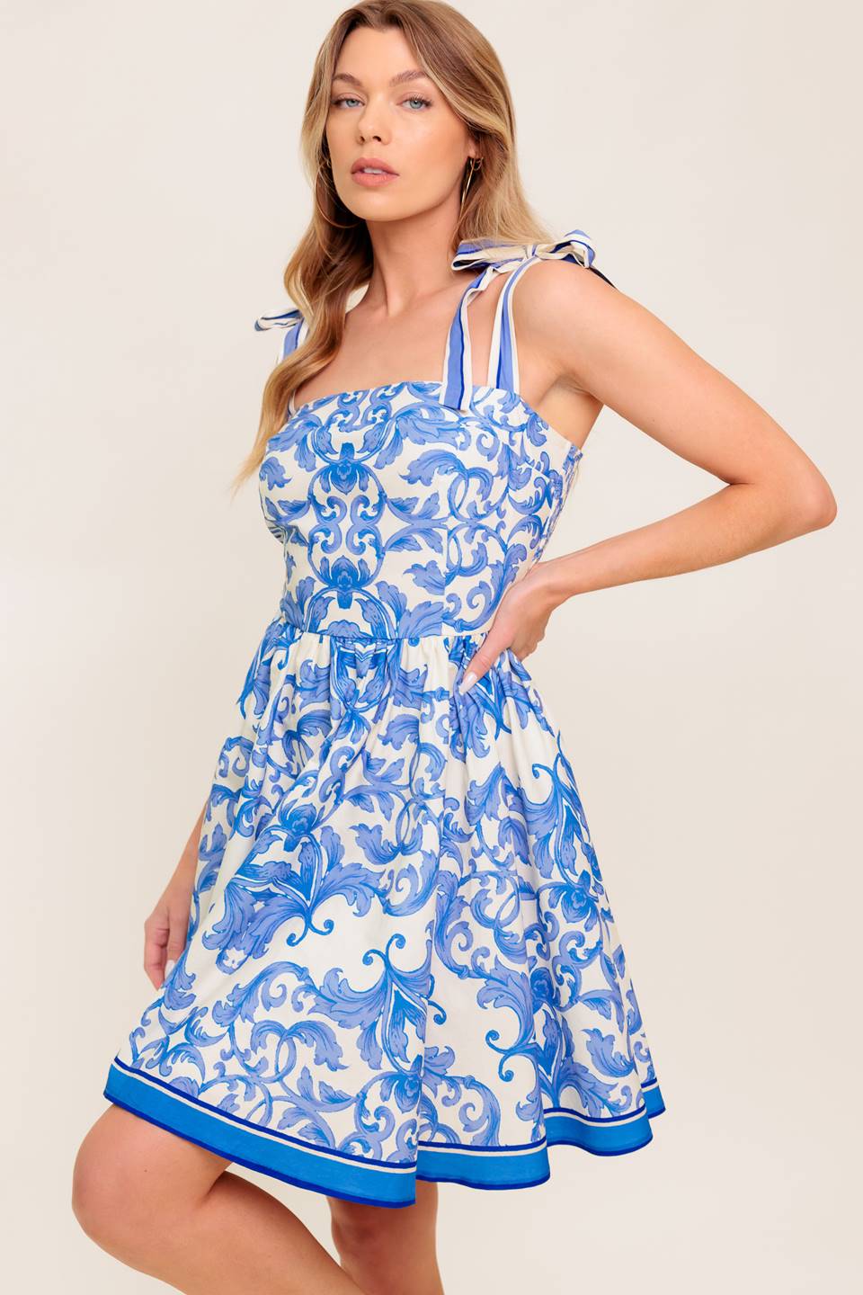 A printed woven mini dress featuring straight neckline, shoulder tie, full skirt and smocked back bodice.