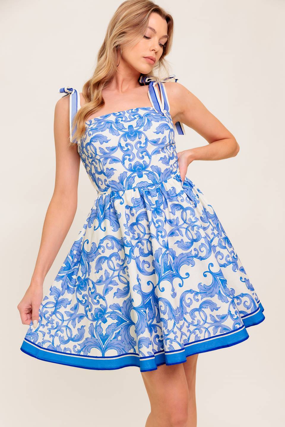 A printed woven mini dress featuring straight neckline, shoulder tie, full skirt and smocked back bodice.