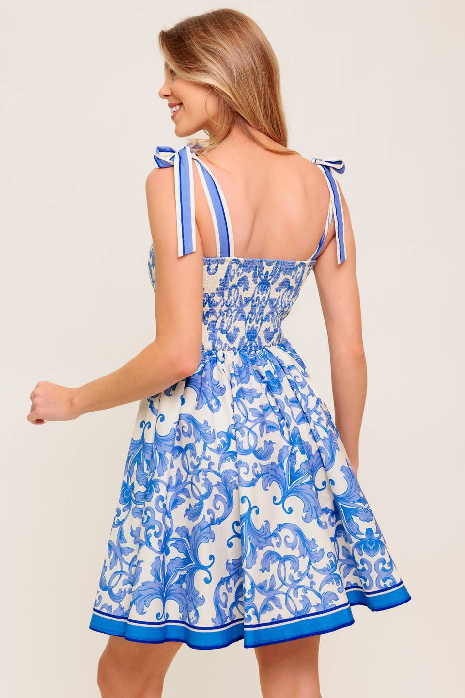 A printed woven mini dress featuring straight neckline, shoulder tie, full skirt and smocked back bodice.