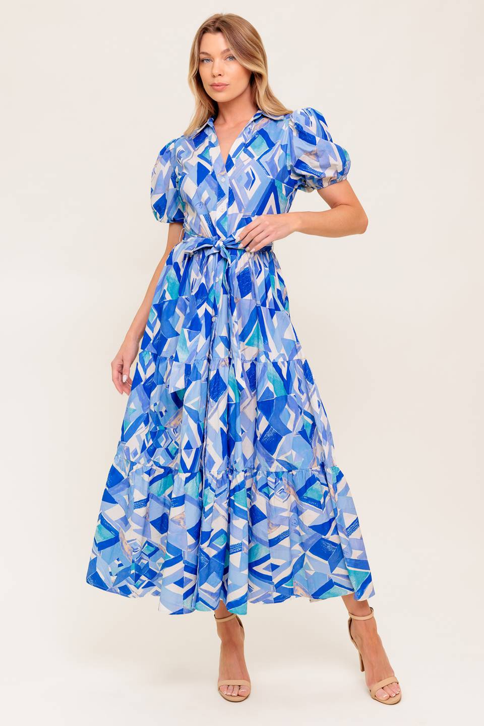 A printed woven midi dress featuring collar, V neck opening, short puff sleeve, front button down closure, self sash tie and tiered skirt.