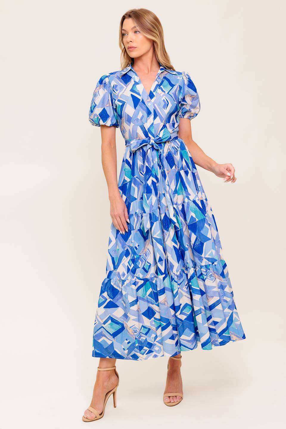 A printed woven midi dress featuring collar, V neck opening, short puff sleeve, front button down closure, self sash tie and tiered skirt.