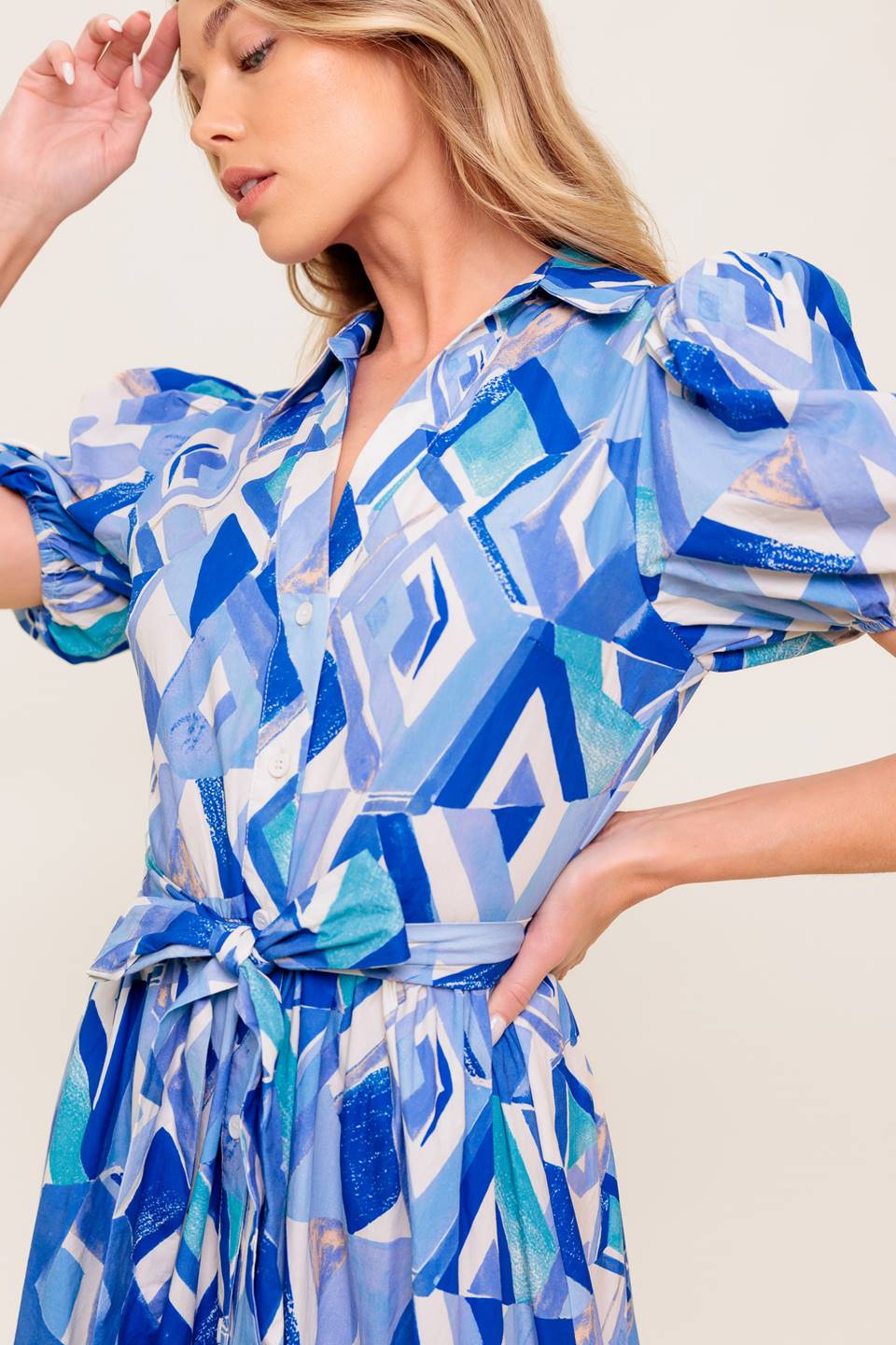 A printed woven midi dress featuring collar, V neck opening, short puff sleeve, front button down closure, self sash tie and tiered skirt.