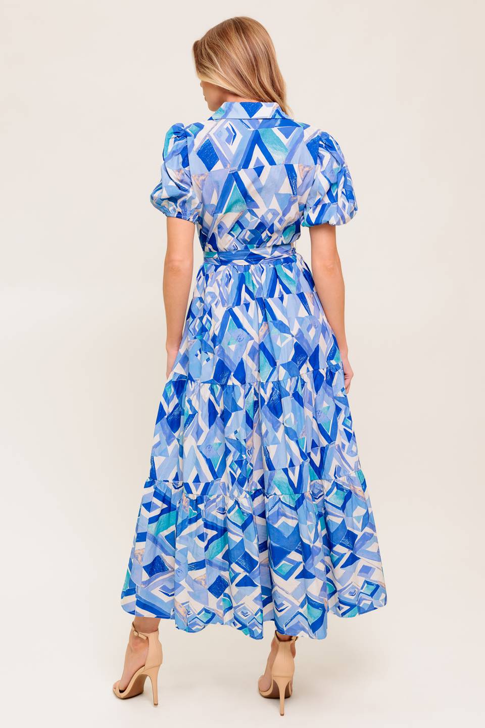 A printed woven midi dress featuring collar, V neck opening, short puff sleeve, front button down closure, self sash tie and tiered skirt.