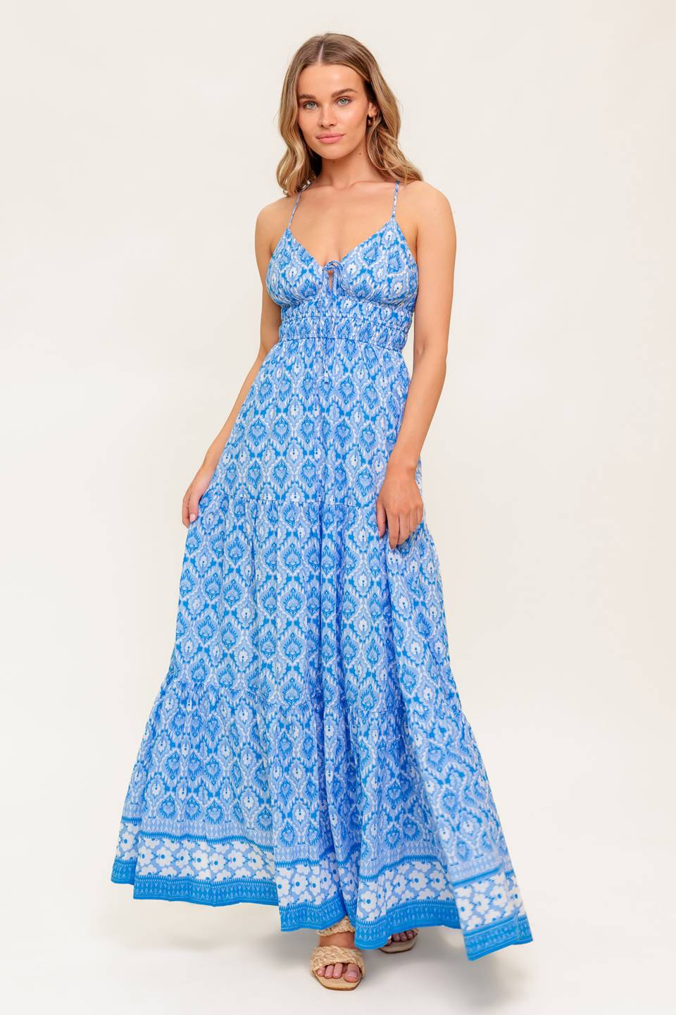 A printed woven maxi dress featuring cami top with center bow, smocked waist, tiered skirt and cross back strap.