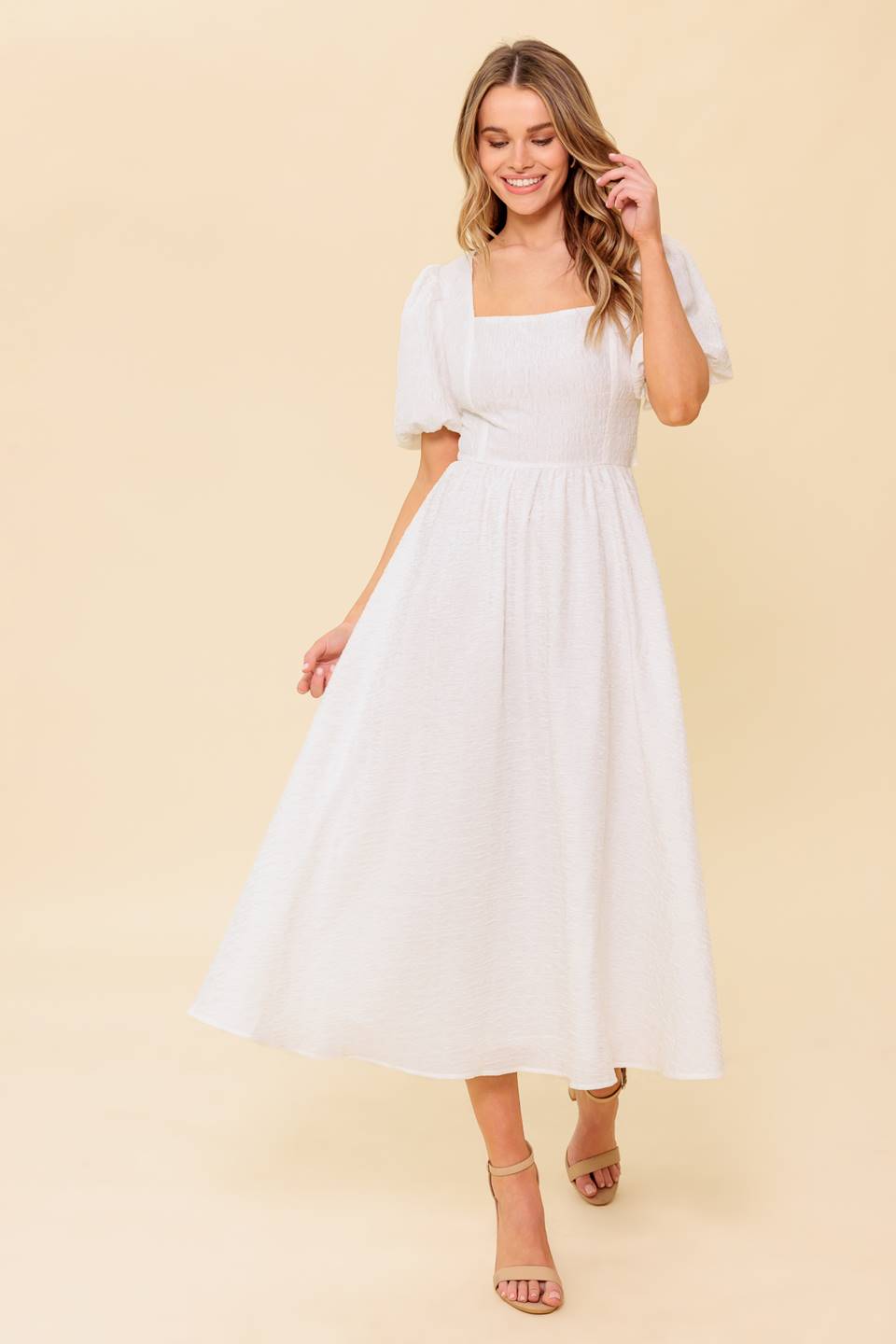 A textured white woven midi dress featuring square neckline, short puff sleeve, full skirt and back button tie closure