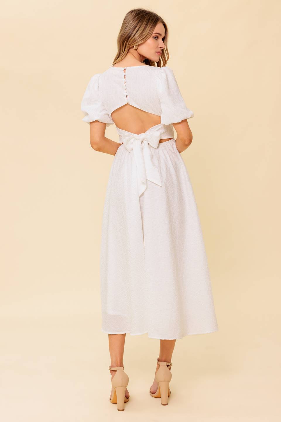 A textured white woven midi dress featuring square neckline, short puff sleeve, full skirt and back button tie closure