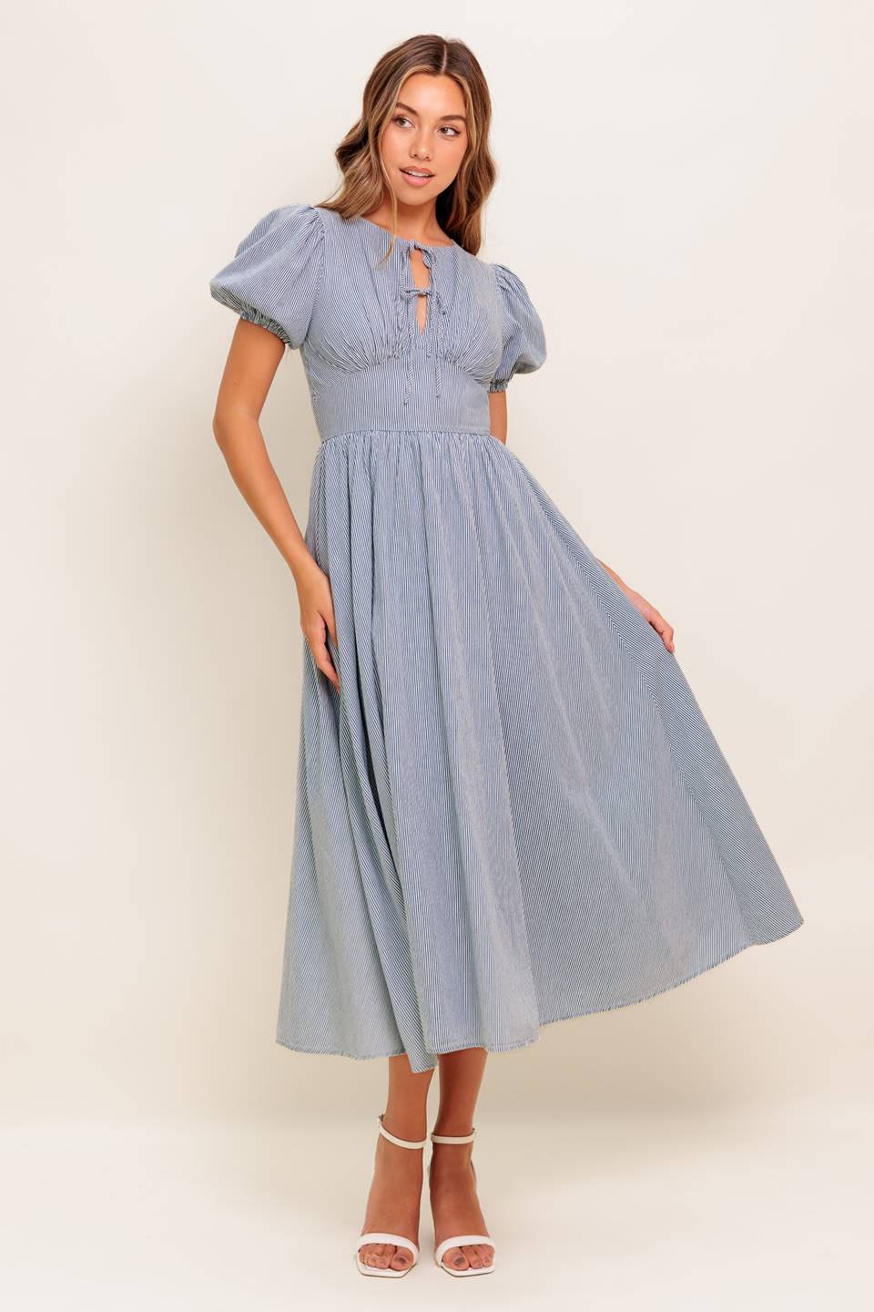 A striped woven midi dress featuring round neckline, front bow ties, short puff sleeve, waist yoke, full skirt and back zipper closure.