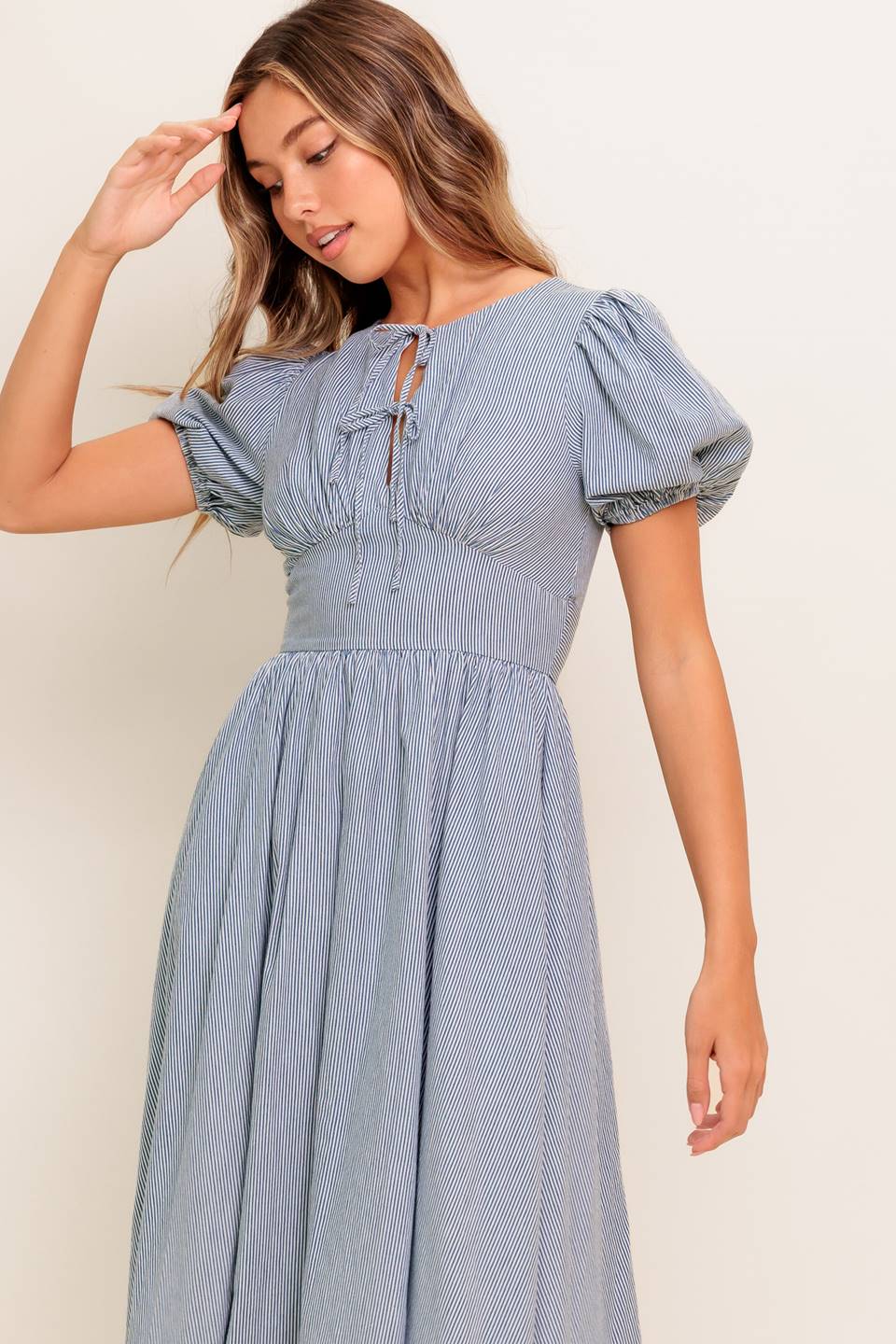 A striped woven midi dress featuring round neckline, front bow ties, short puff sleeve, waist yoke, full skirt and back zipper closure.