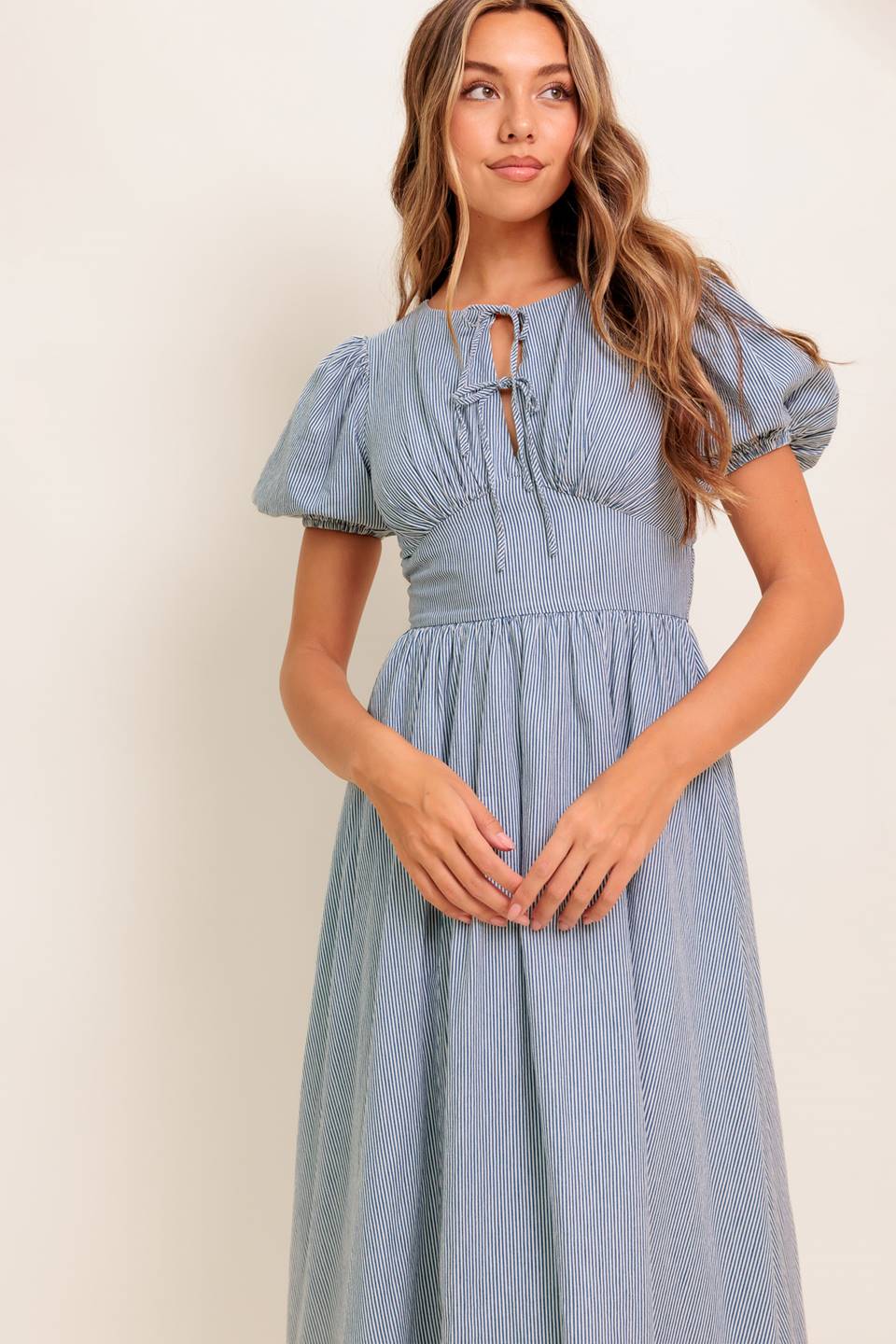 A striped woven midi dress featuring round neckline, front bow ties, short puff sleeve, waist yoke, full skirt and back zipper closure.