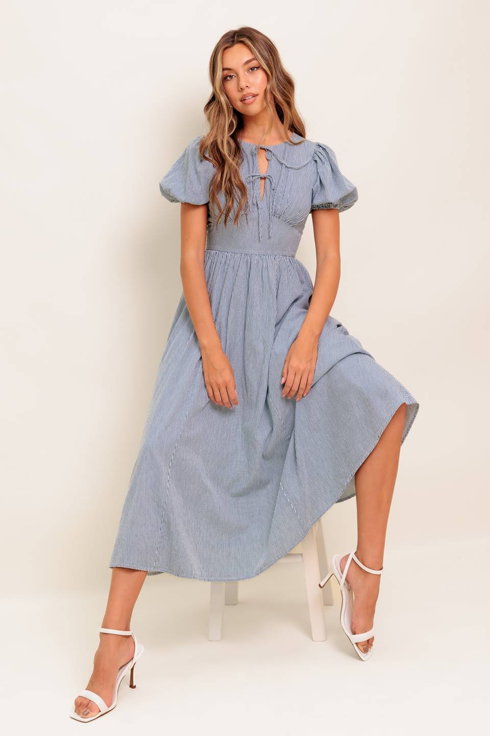 A striped woven midi dress featuring round neckline, front bow ties, short puff sleeve, waist yoke, full skirt and back zipper closure.