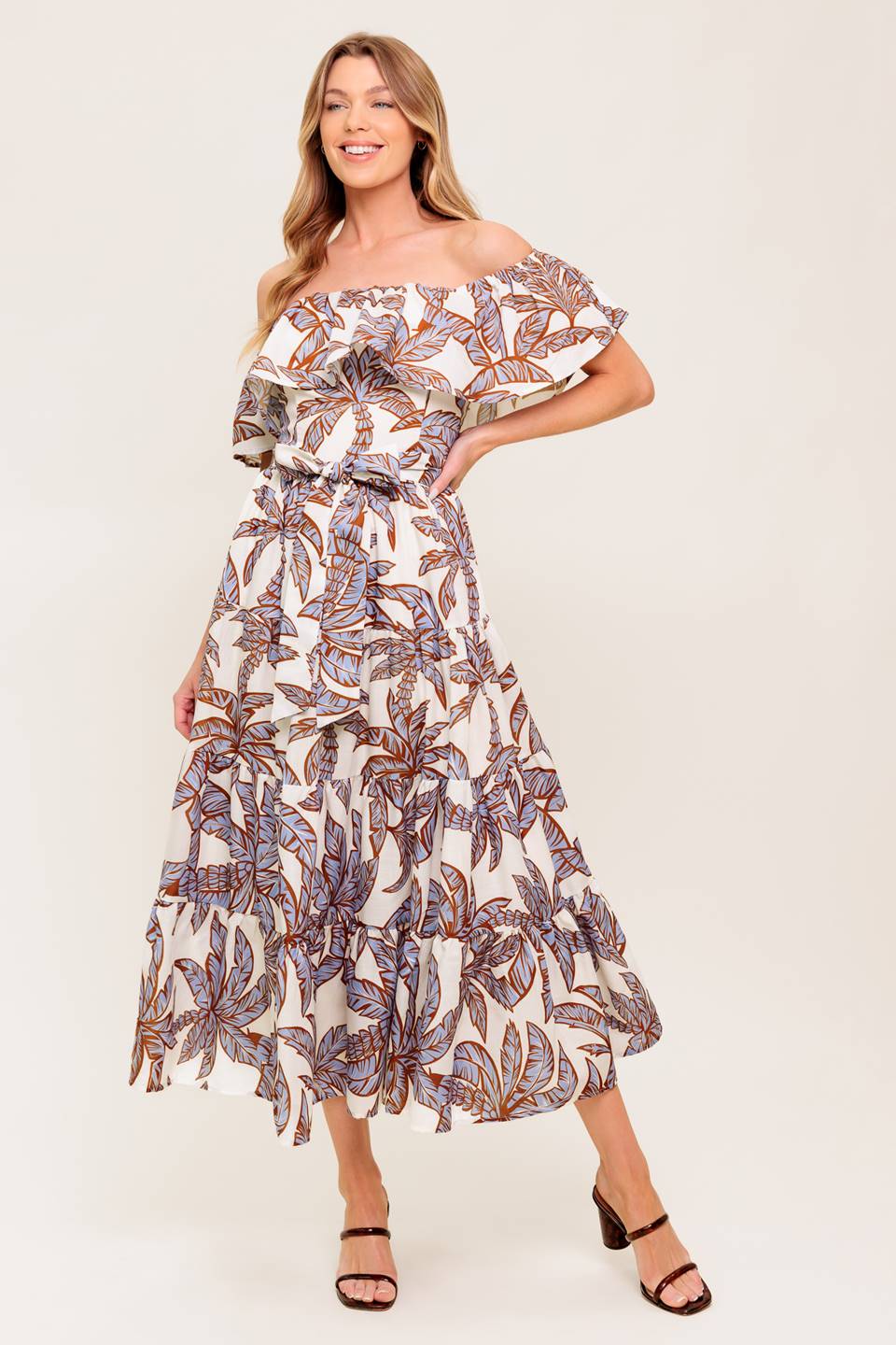 A printed woven midi dress featuring off shoulder neckline, flounce, elasticized waist with self sash tie and tiered skirt.