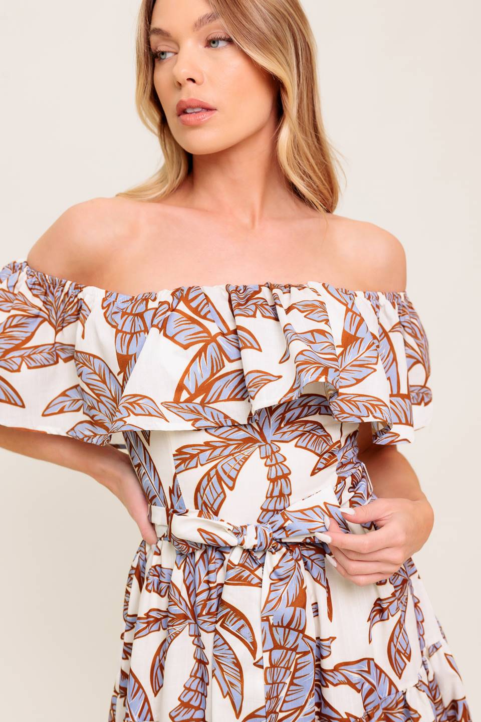A printed woven midi dress featuring off shoulder neckline, flounce, elasticized waist with self sash tie and tiered skirt.