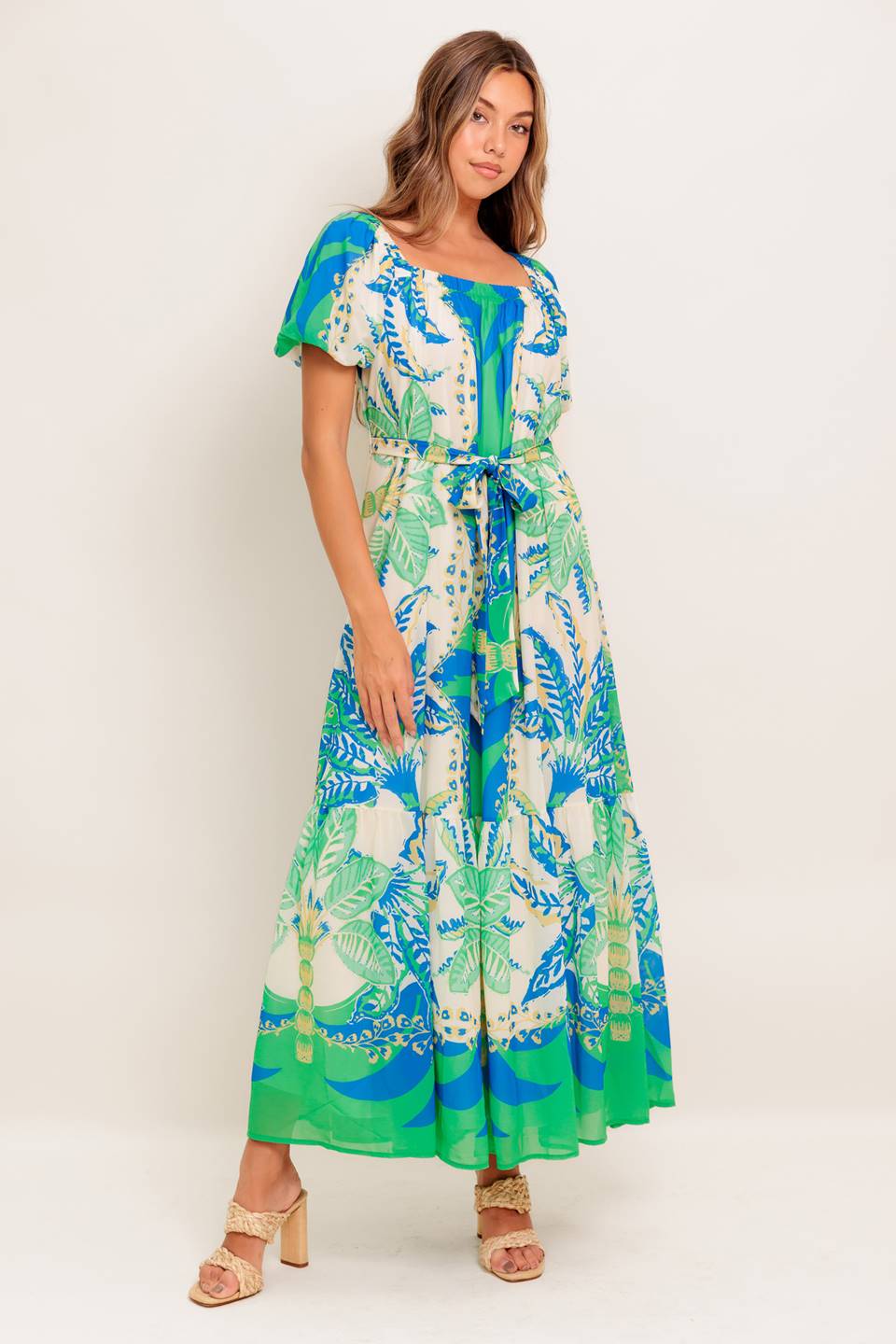 A printed woven maxi dress featuring square neckline, short puff sleeve, self sash tie and ruffled hemline