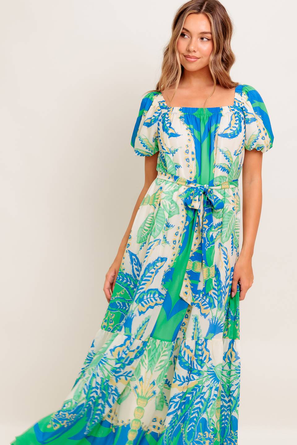 A printed woven maxi dress featuring square neckline, short puff sleeve, self sash tie and ruffled hemline