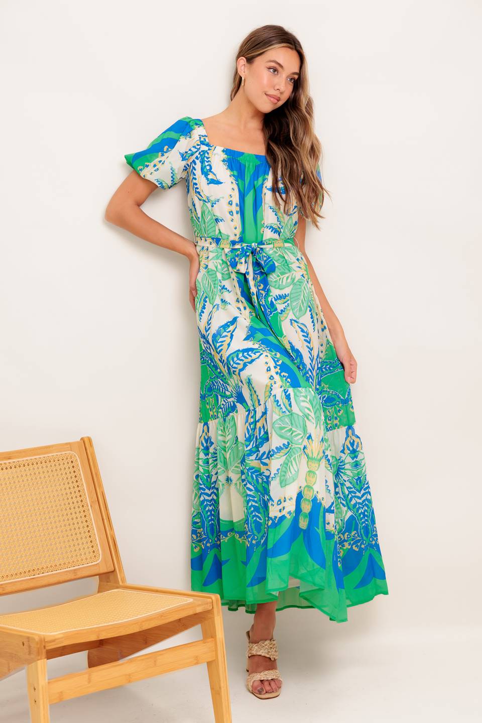 A printed woven maxi dress featuring square neckline, short puff sleeve, self sash tie and ruffled hemline