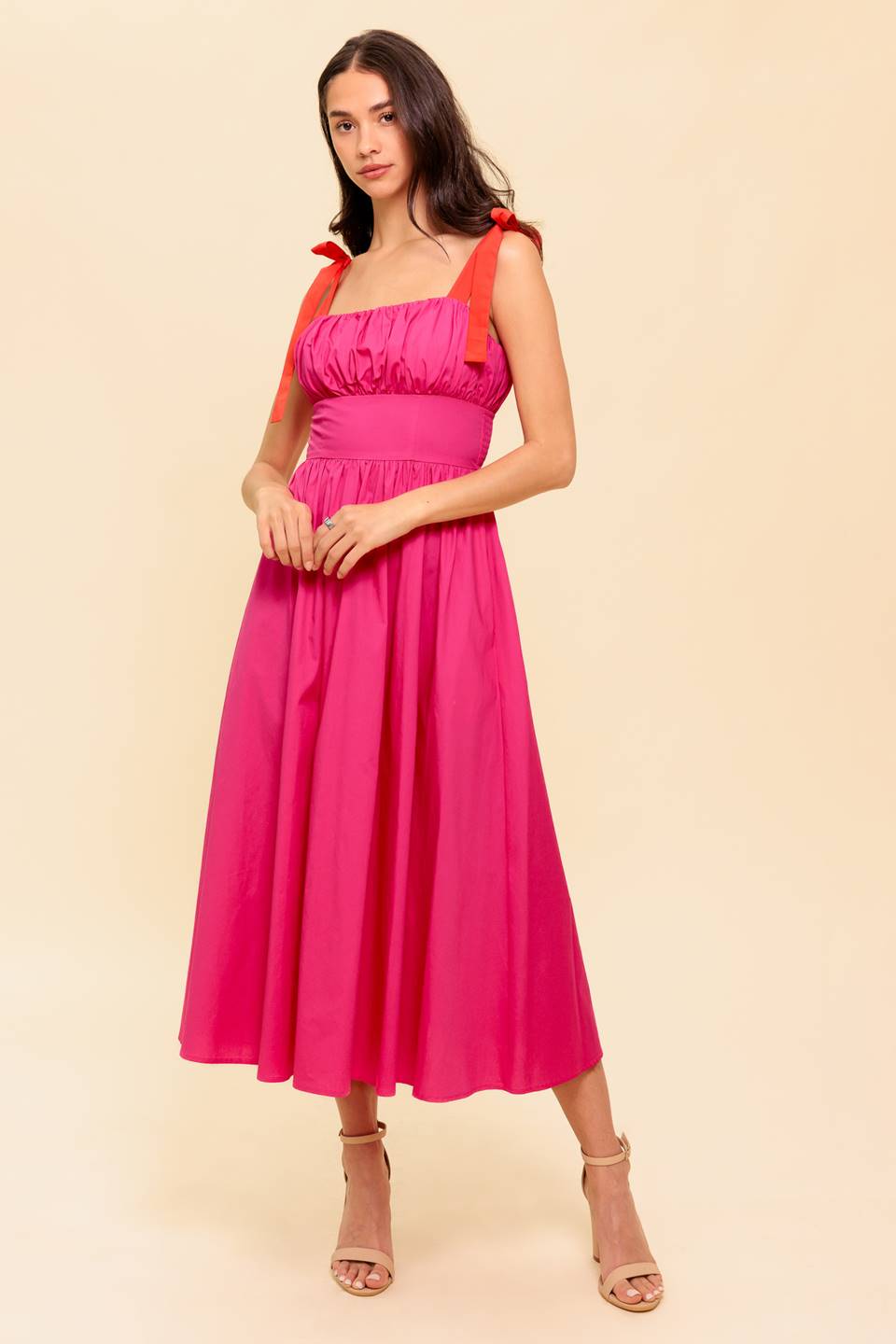 A solid fuchsia woven midi dress featuring straight neckline, red self-tie straps, shirred bodice, full skirt and smocked back bodice and zipper closure
