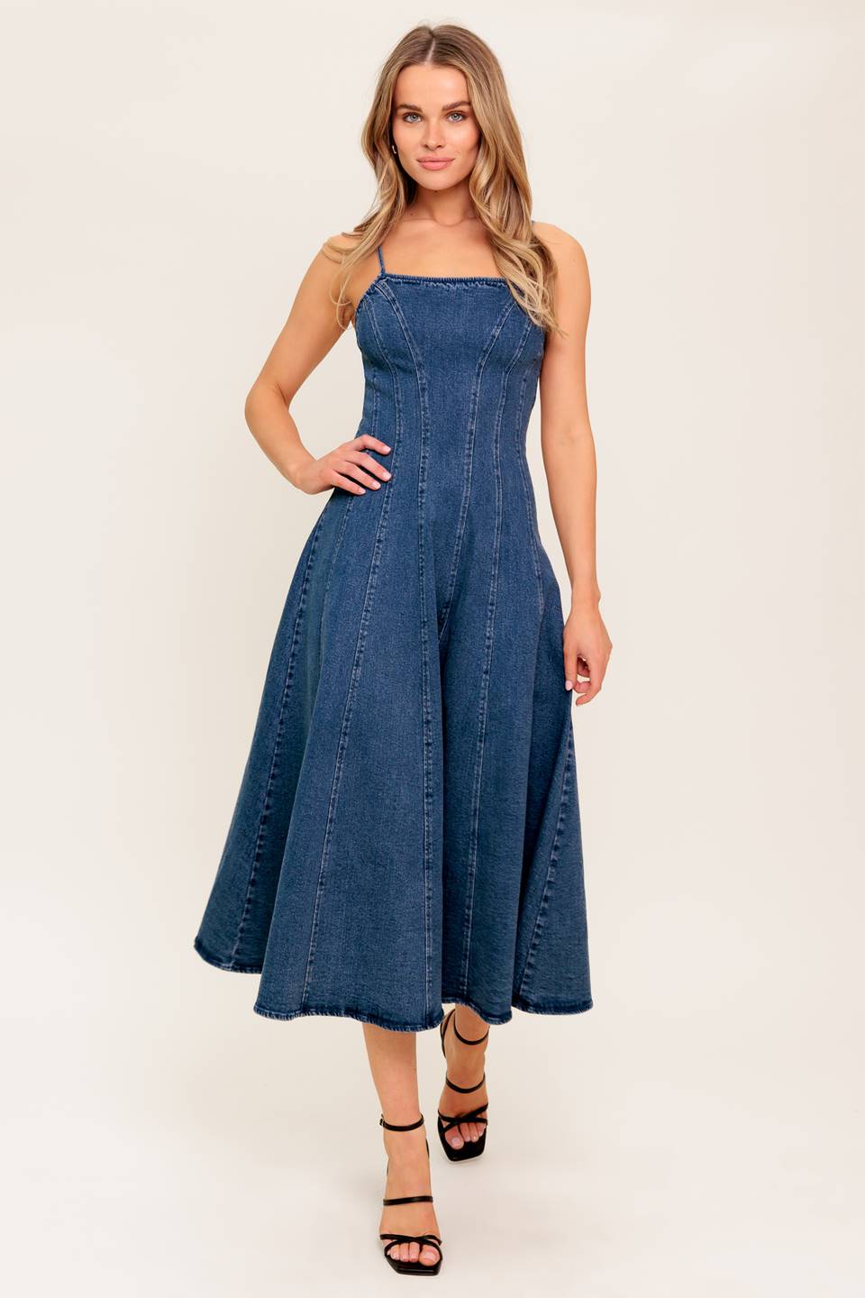 A dark-washed denim midi dress featuring a straight neckline, straps, full skirt and back zipper closure.