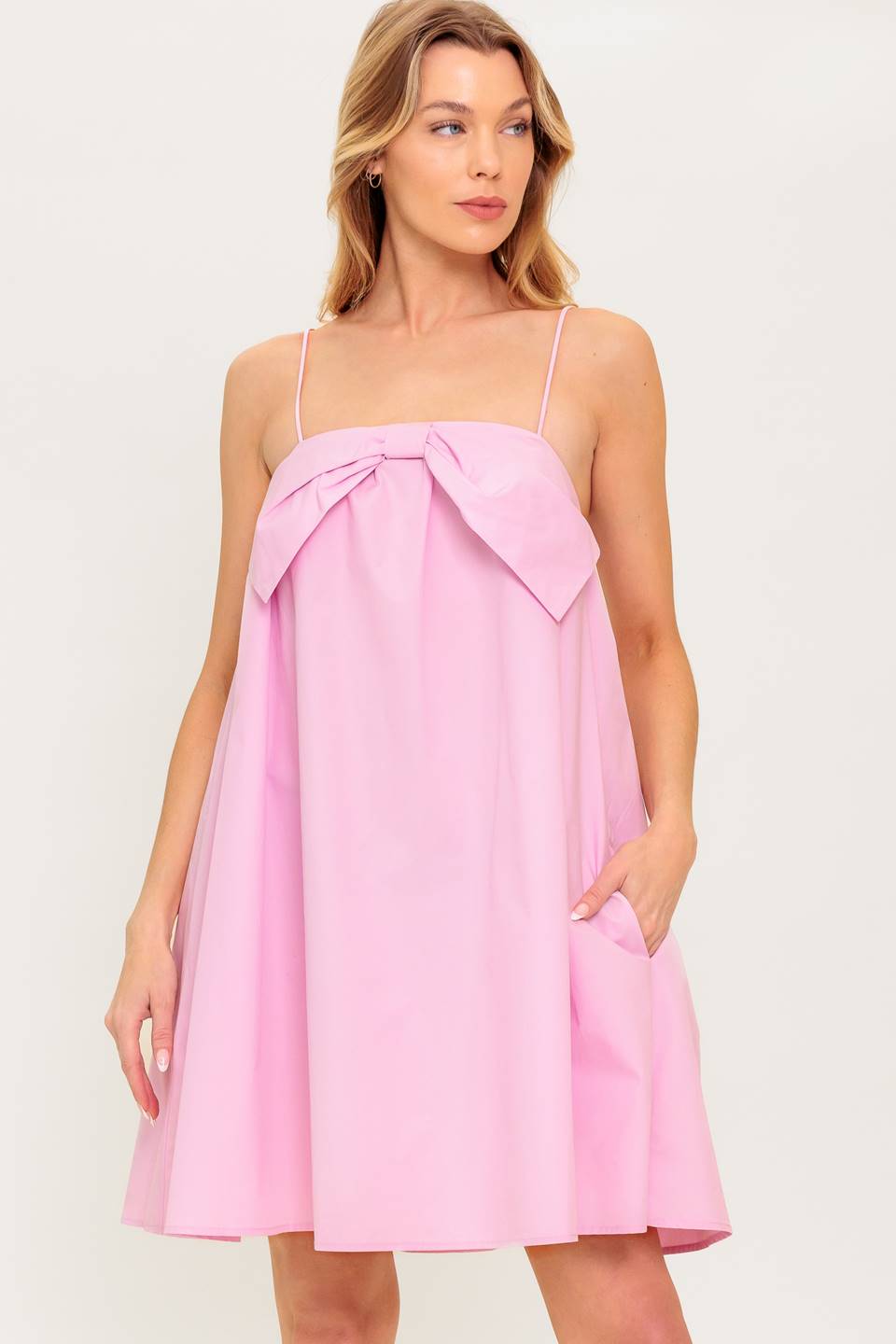 A pink solid woven mini dress featuring straight neckline, front bow detail and elasticized back