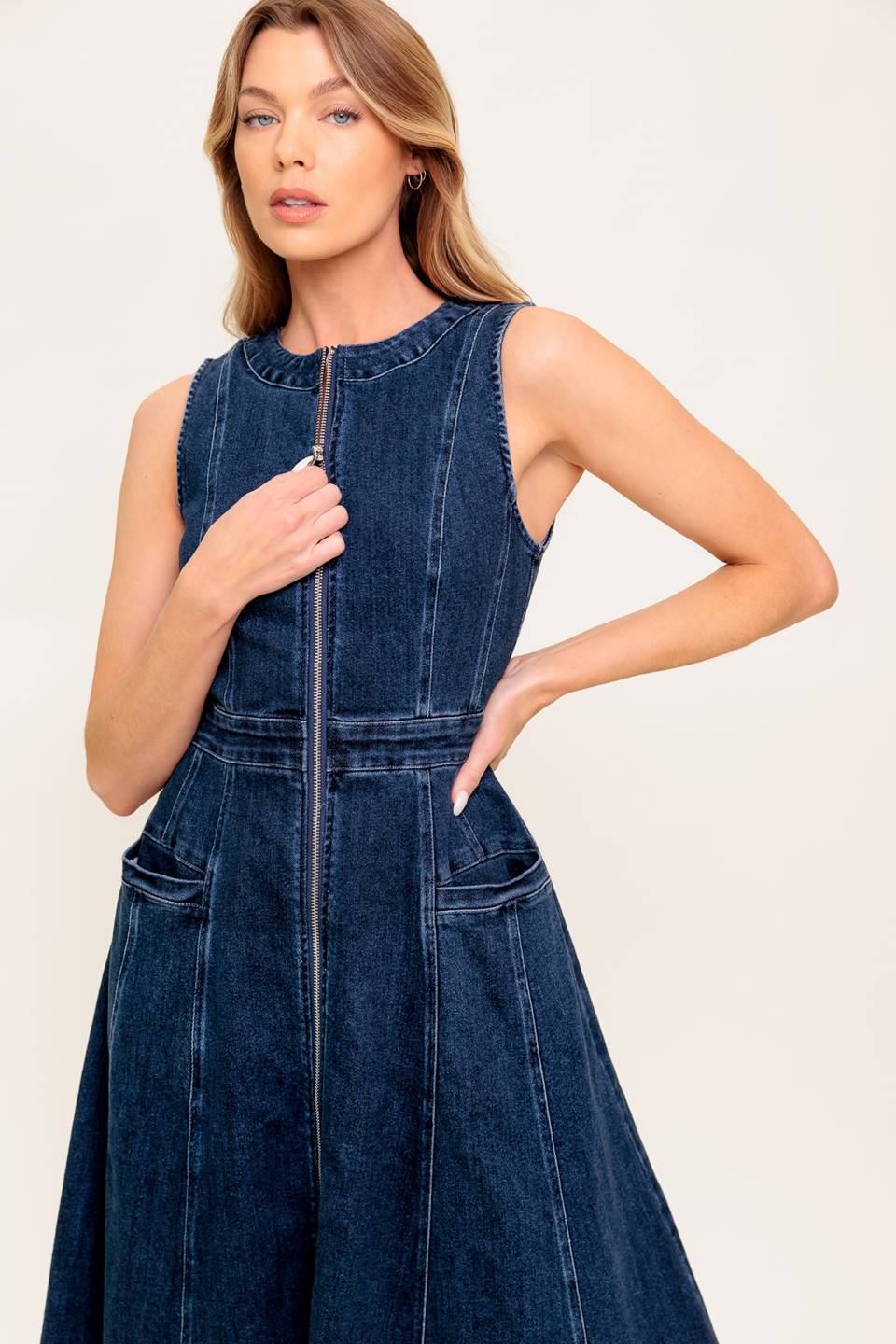 A washed denim midi dress featuring round neckline, sleeveless, front zipper closure, side pocket and circle skirt.