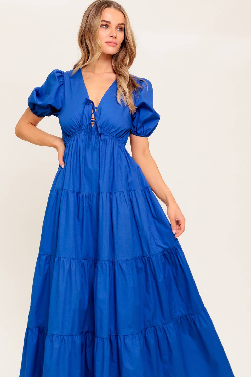 A solid royal blue woven maxi dress featuring V neckline with front bow closure, short puff sleeve, elasticized empire and tiered skirt.