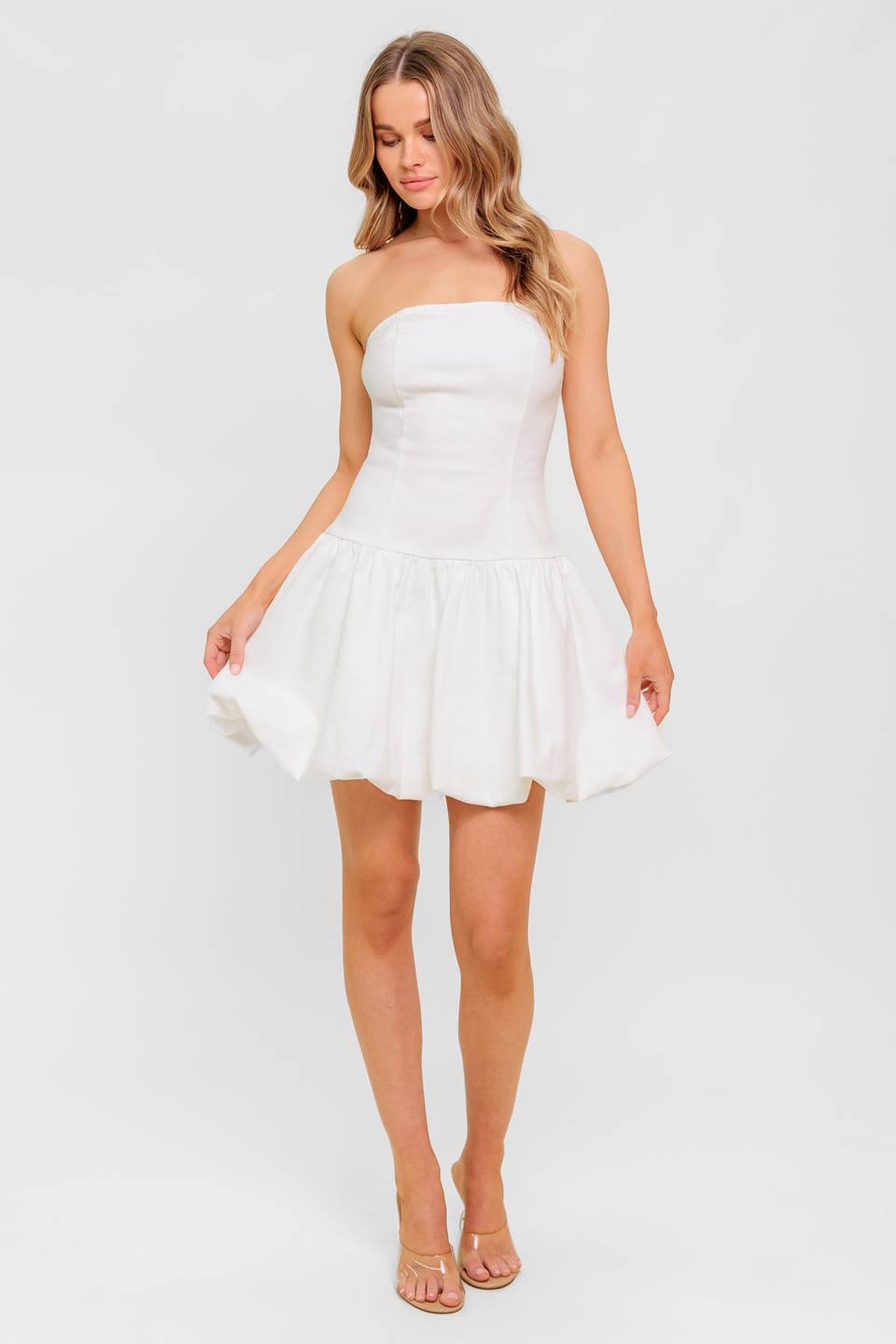 A solid woven twill mini dress featuring strapless, drop waist, bubble hemline and back zipper closure