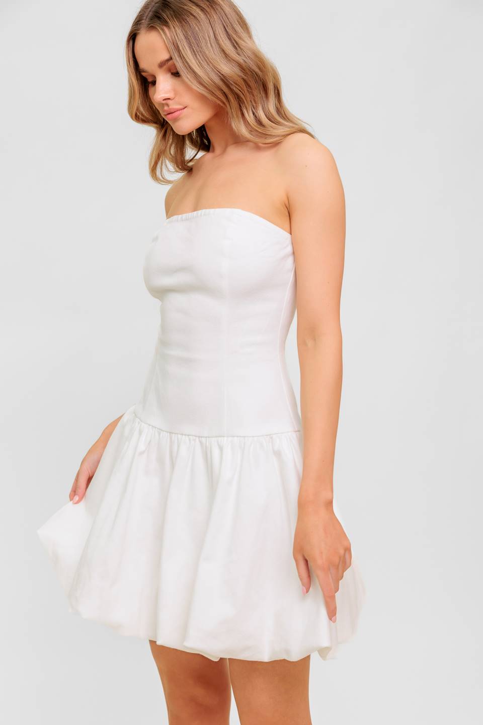 A solid woven twill mini dress featuring strapless, drop waist, bubble hemline and back zipper closure