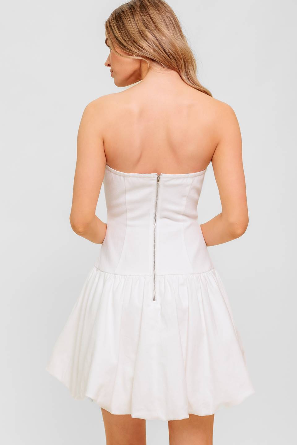 A solid woven twill mini dress featuring strapless, drop waist, bubble hemline and back zipper closure