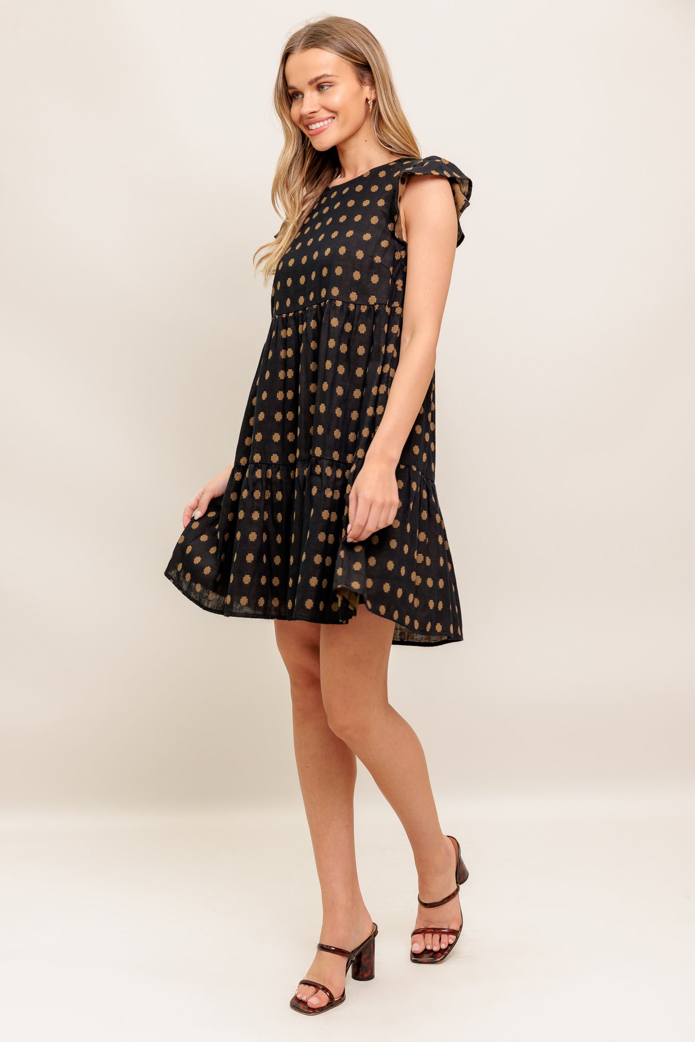 A textured woven mini dress featuring round neckline, ruffled sleeve, tiered body and back neck button closure