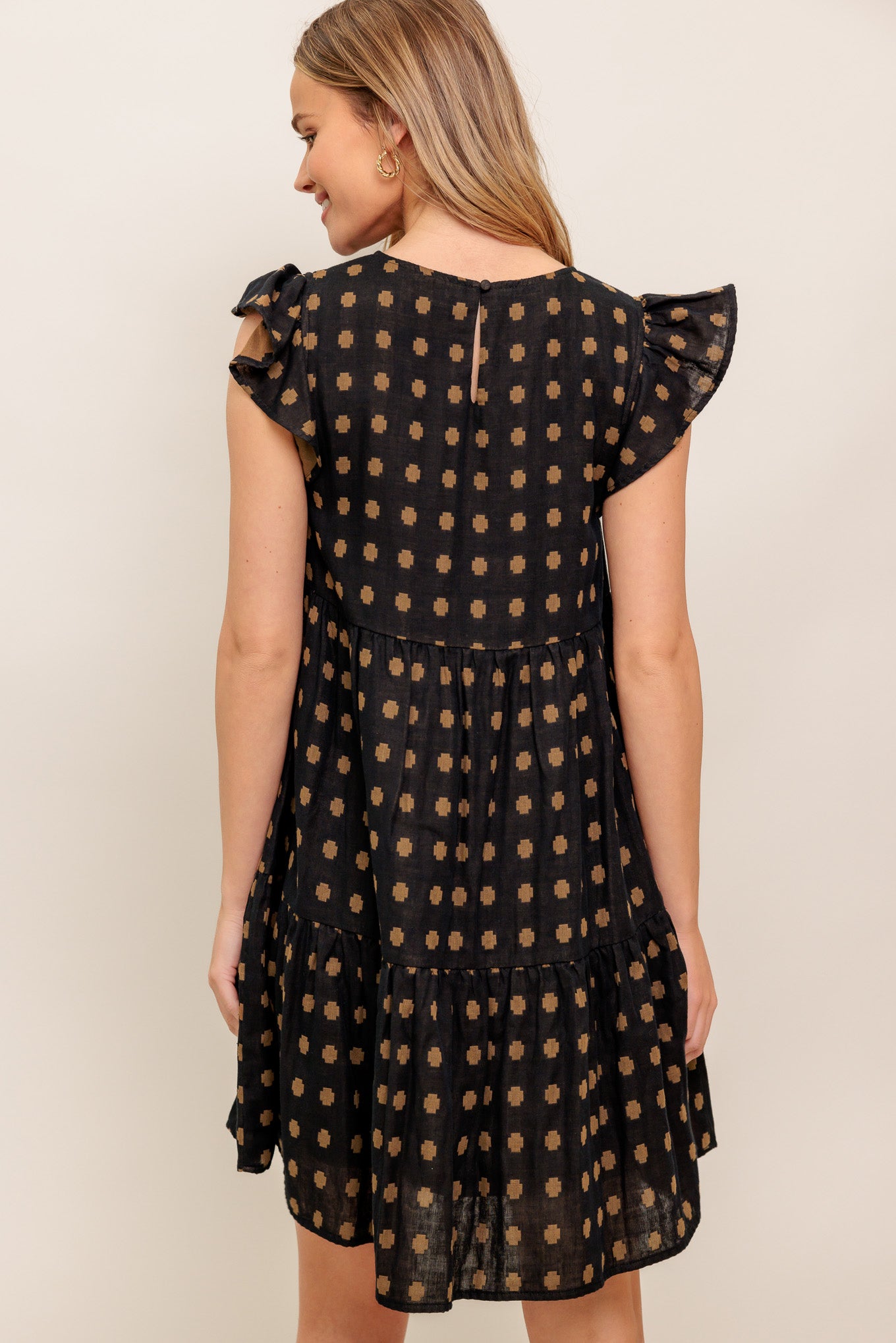 A textured woven mini dress featuring round neckline, ruffled sleeve, tiered body and back neck button closure