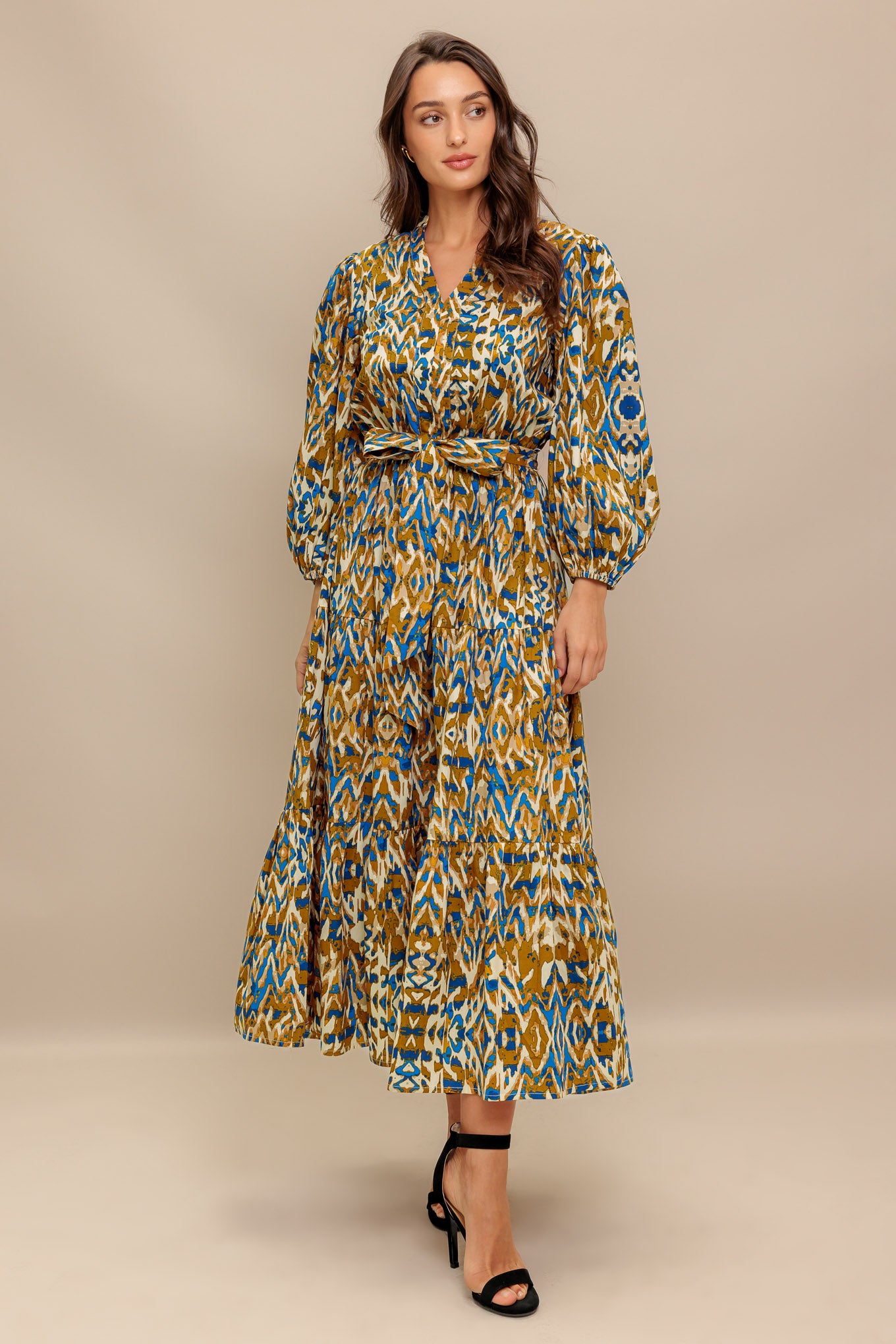 A printed woven midi dress featuring V neckline, 3/4 sleeve, elasticized waist with self sash and tiered skirt