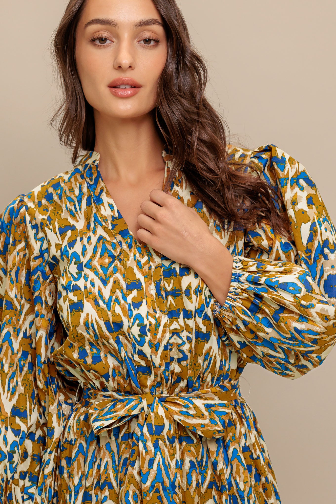 A printed woven midi dress featuring V neckline, 3/4 sleeve, elasticized waist with self sash and tiered skirt