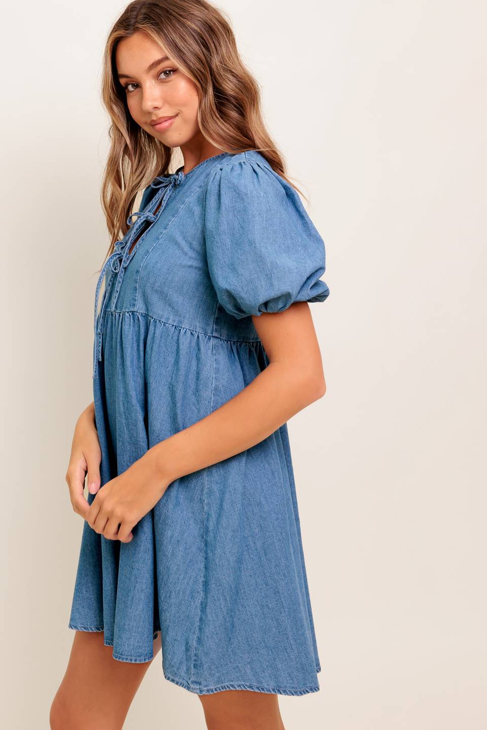 A washed denim mini dress featuring round neckline, front bow ties and short puff sleeve