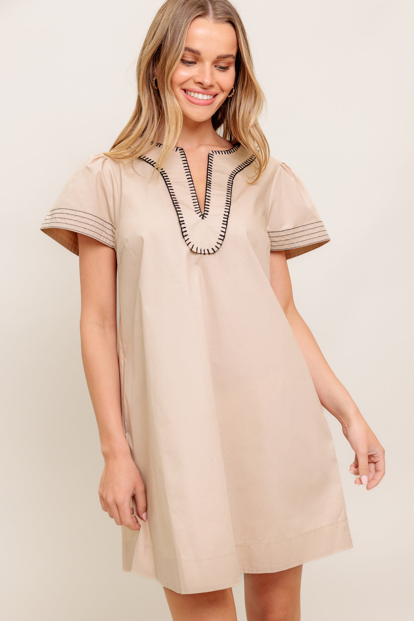 A solid woven mini dress featuring round neckline with V center and embroidered edge and short bell sleeve