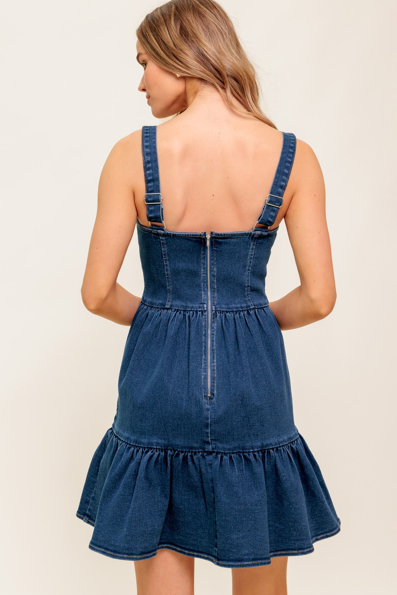 A washed denim mini dress featuring bustier top, straps, button down, ruffled hemline and back zipper closure.